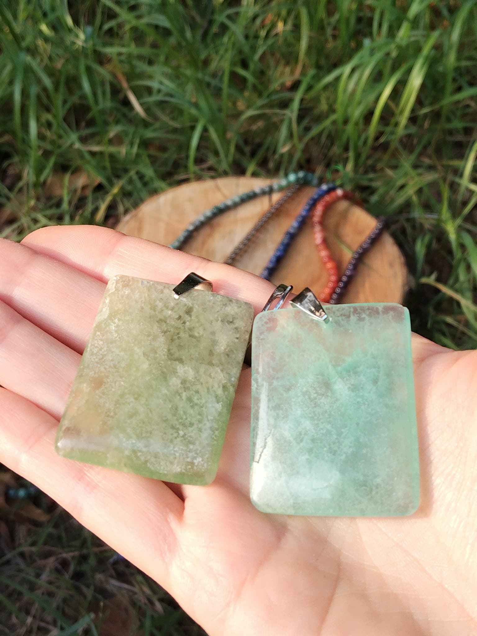 Pendentif fluorite verte rectangulaire tenu dans la main devant l’herbe, bijou en pierre naturelle évoquant le recentrage, la douceur du cœur et la lucidité.