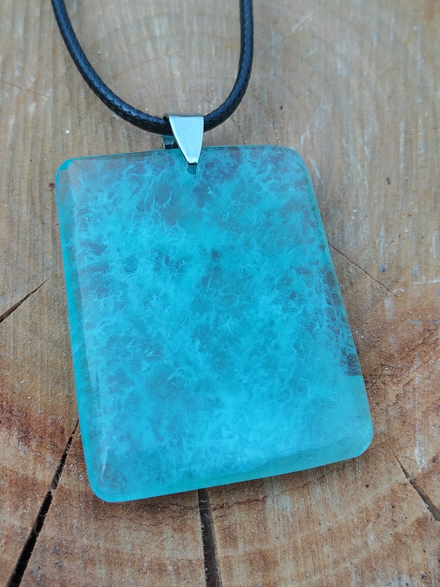 Zoom sur pendentif en fluorite verte rectangulaire monté sur cordon noir, fond bois naturel, pierre naturelle associée au recul, à la fraîcheur mentale et à l’harmonie intérieure.