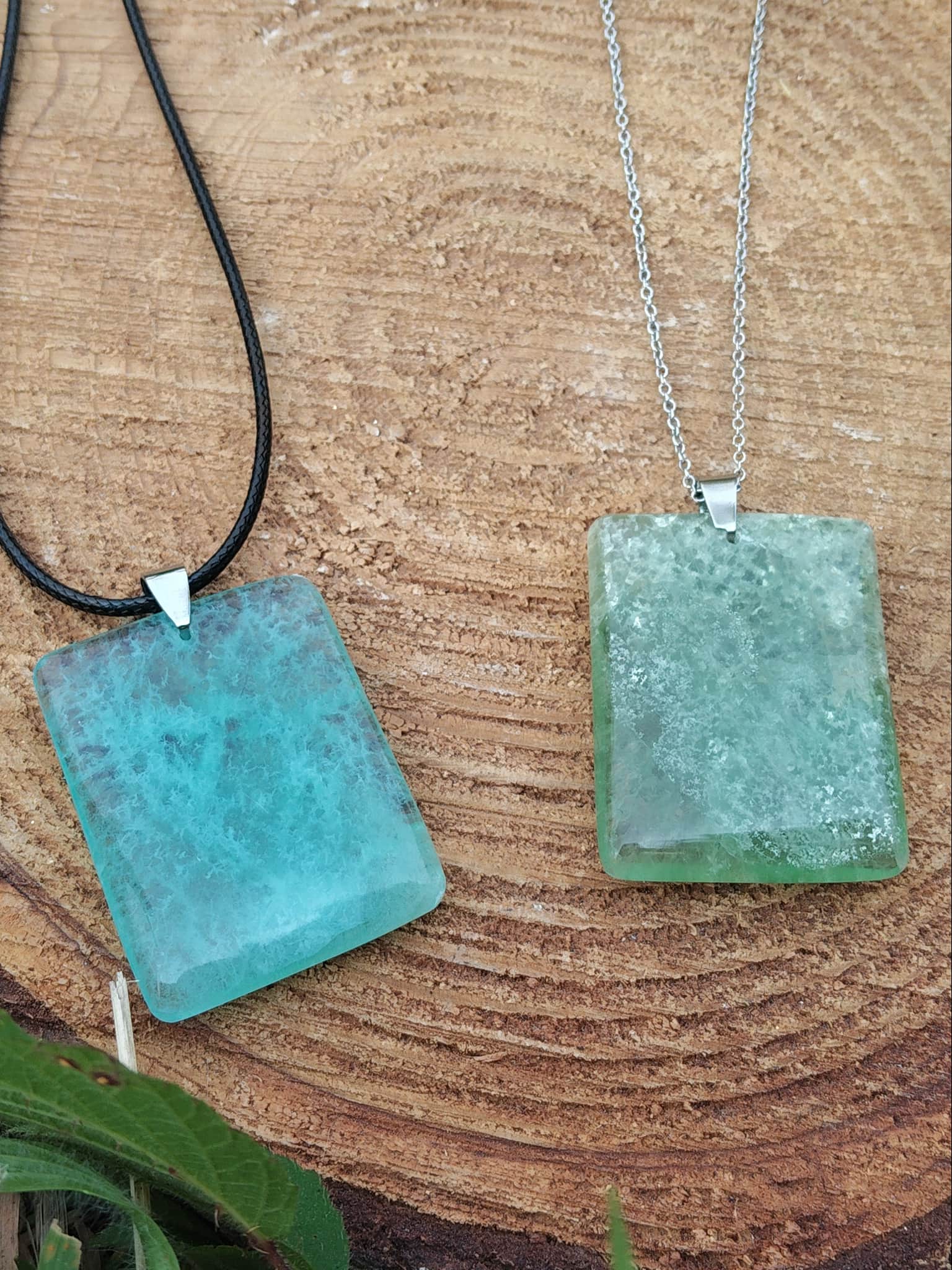 Pendentif fluorite verte rectangulaire sur cordon noir et chaîne argentée posé sur tranche de bois, bijou en pierre naturelle associé à la fraîcheur du mental, à la douceur et à la stabilité intérieure.