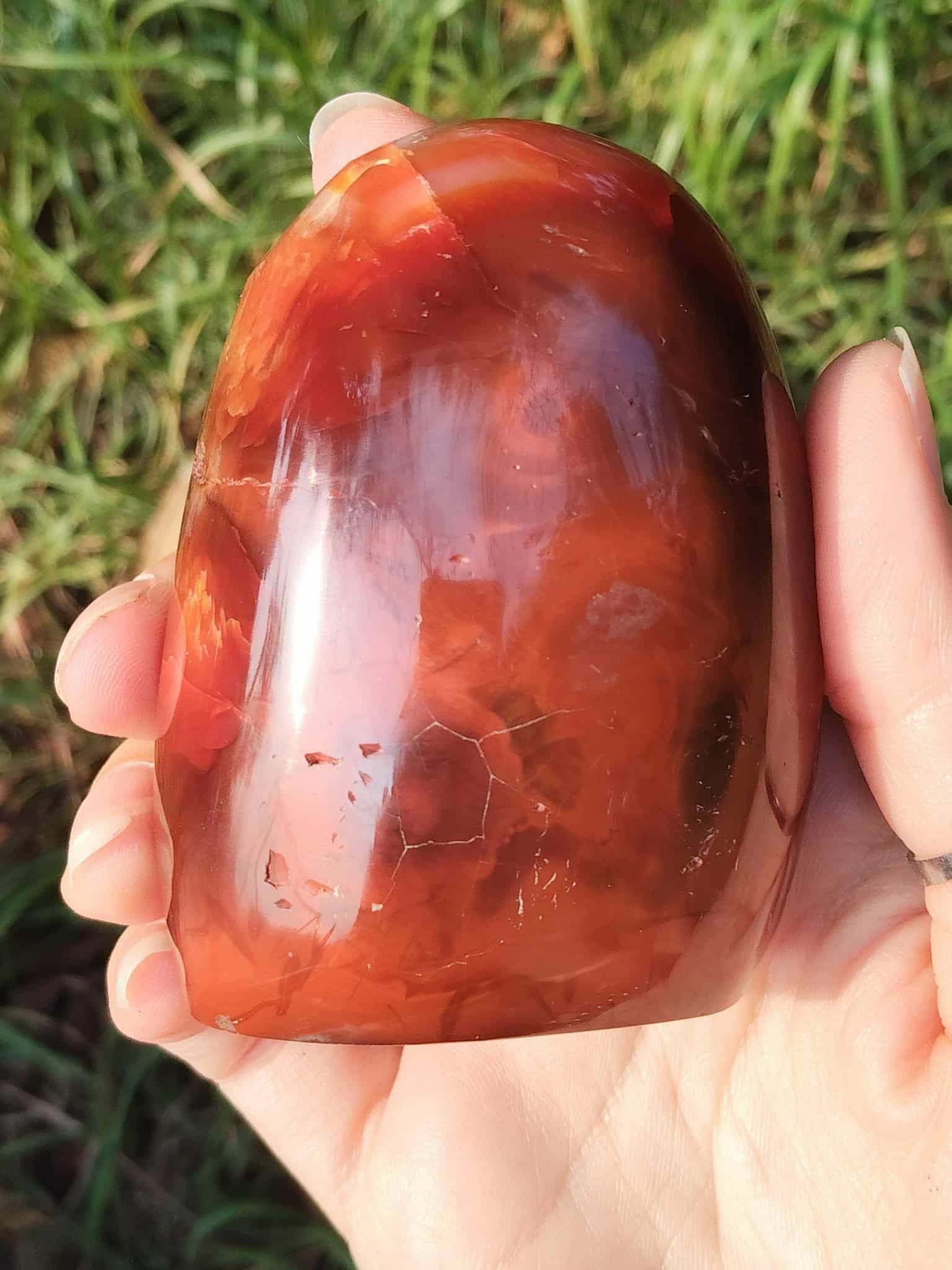 Forme libre Cornaline naturelle tenue dans la main en extérieur, pierre orange-rouge polie – soutien énergétique de vitalité, créativité et équilibre émotionnel.