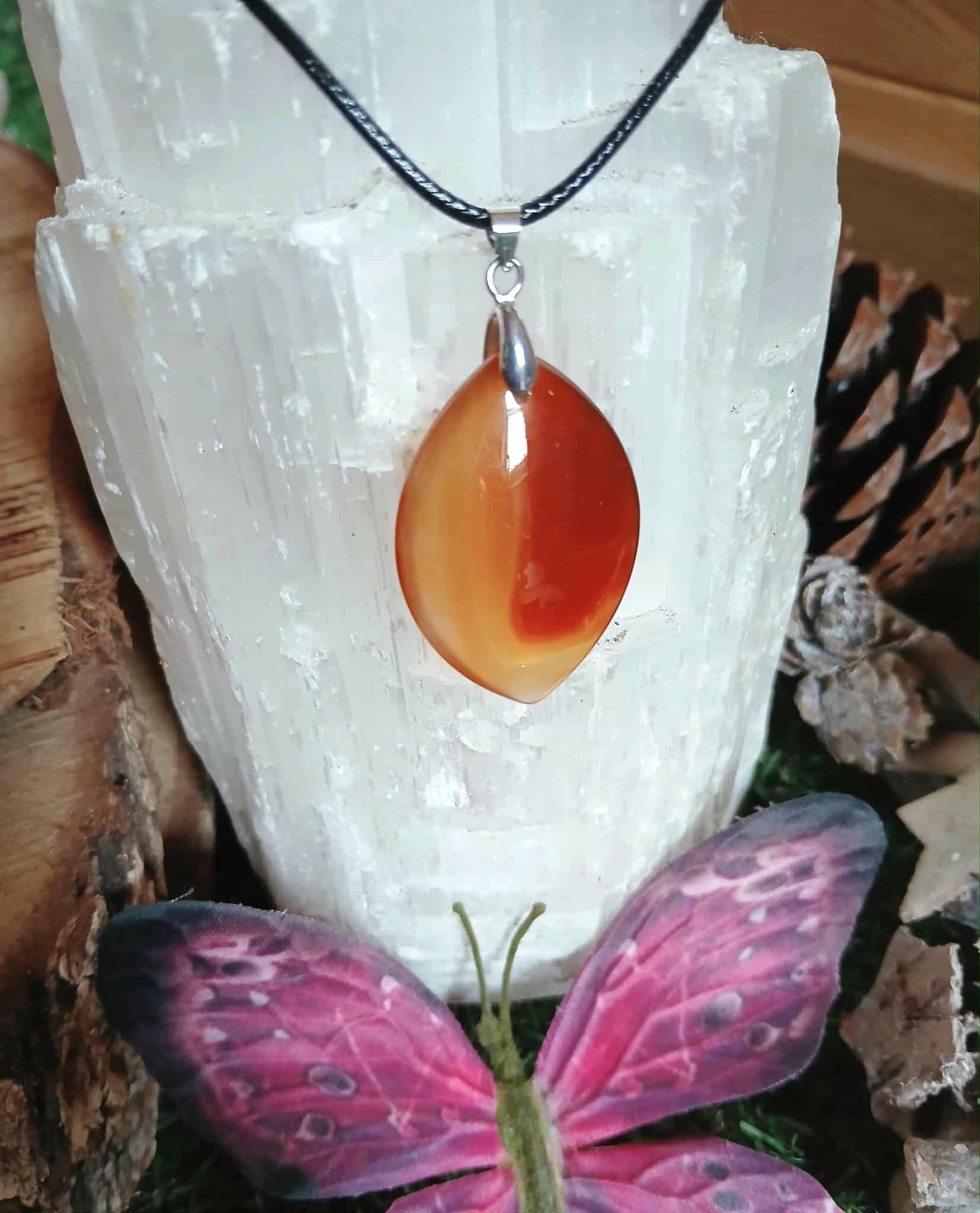 Pendentif Cornaline naturelle sur cordon noir, exposé sur une sélénite avec papillon, bijou énergétique pour vitalité, créativité et concentration.