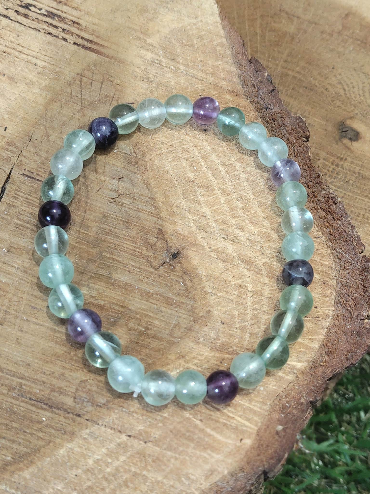 Bracelet fluorite verte et violette en perles naturelles vu du dessus sur rondin de bois, bijou Magic Gaïa pour clarté mentale et apaisement émotionnel.