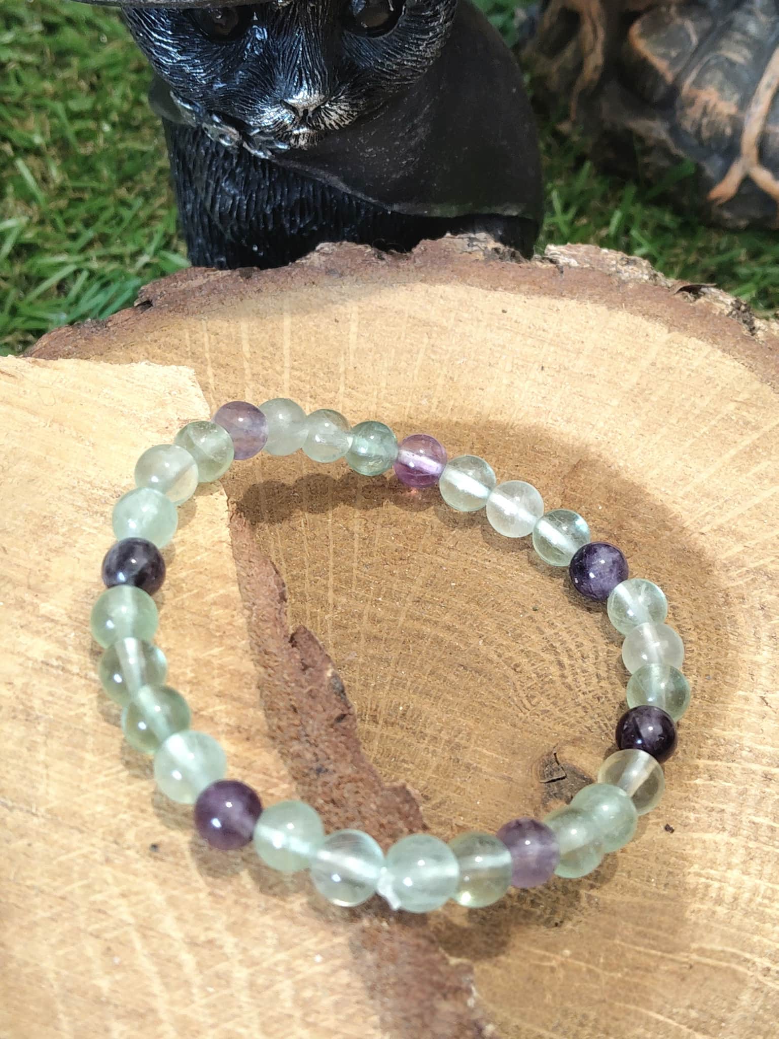 Bracelet fluorite verte et violette en pierres naturelles posé sur rondin de bois, bijou de lithothérapie Magic Gaïa pour clarté mentale et équilibre émotionnel.