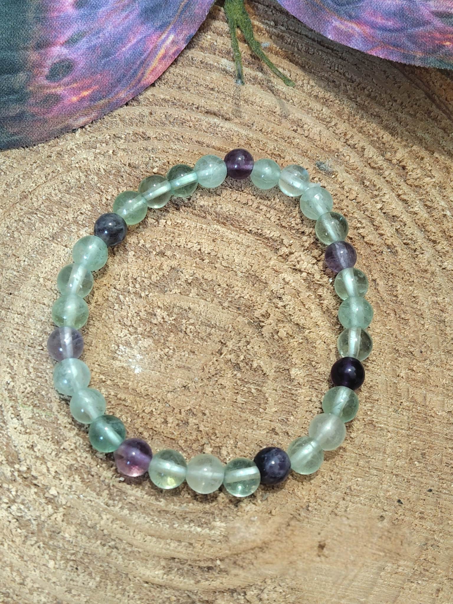 Bracelet fluorite verte et violette en pierres naturelles vu du dessus sur rondin de bois, bijou Magic Gaïa de lithothérapie pour équilibre du cœur et de l’esprit.