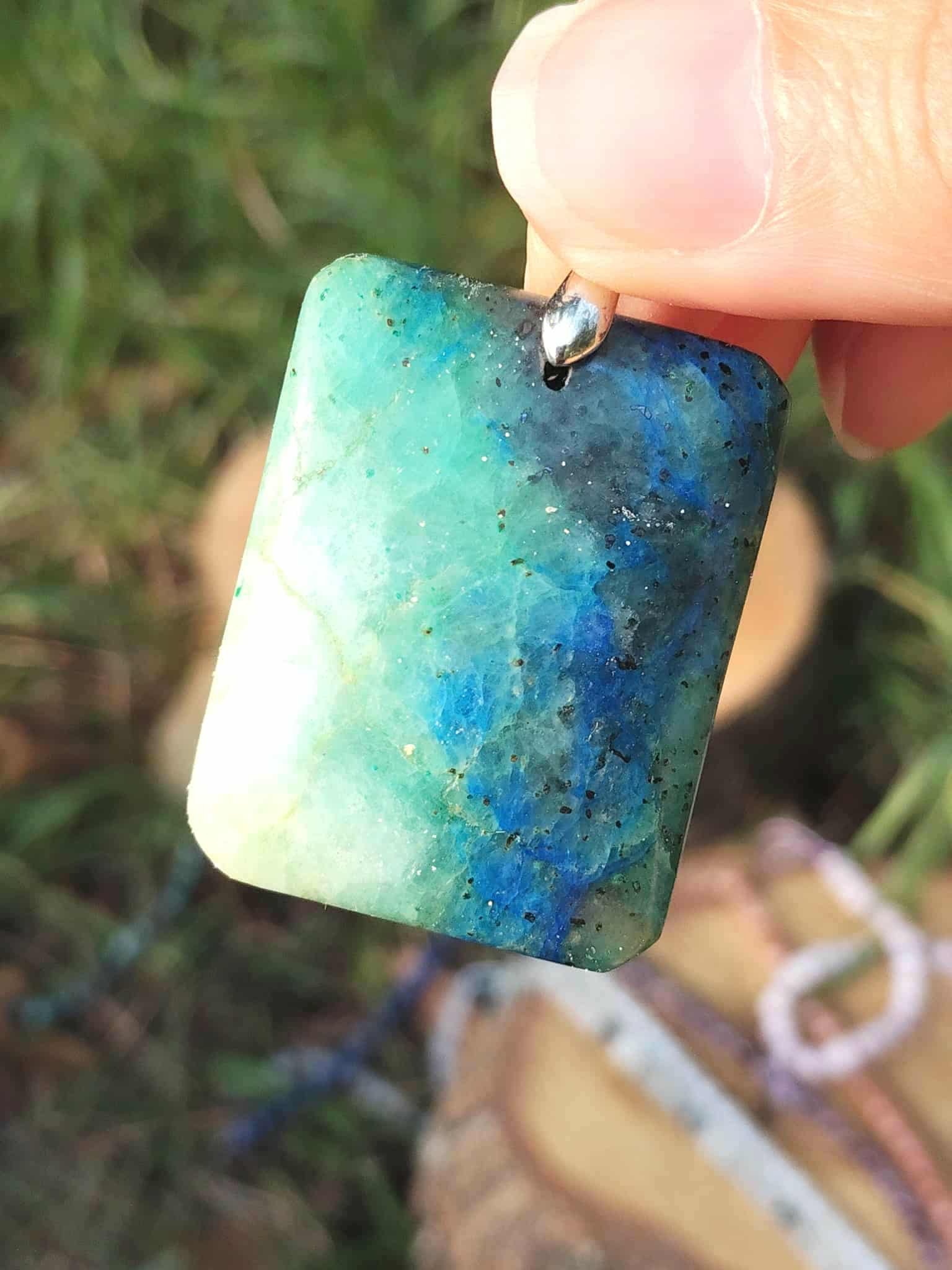 Pendentif azurite chrysocolle bleu vert tenu entre les doigts, bijou en pierre naturelle associé au recul, à la sensibilité maîtrisée et à la justesse d’expression.