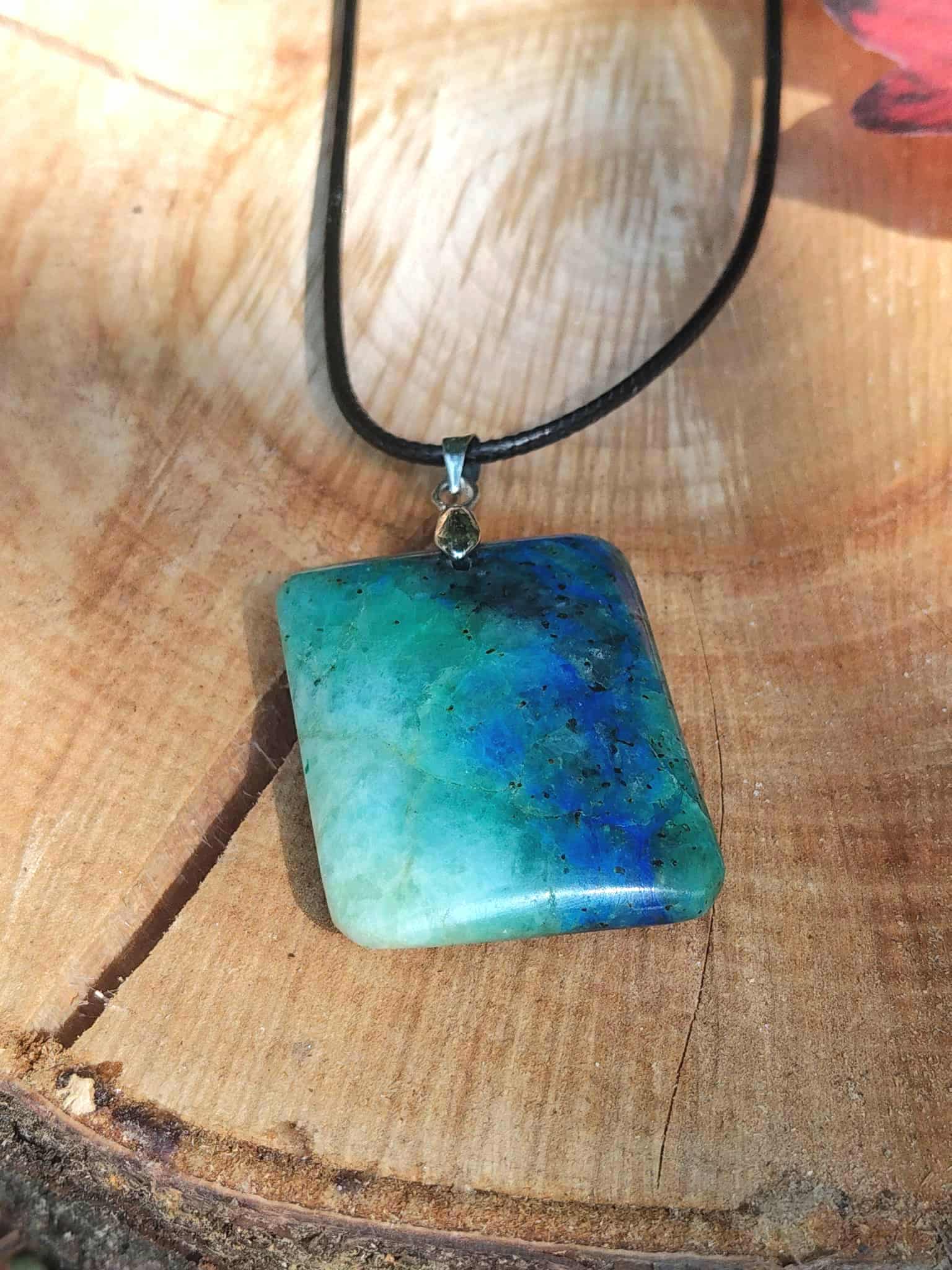 Pendentif azurite chrysocolle bleu vert sur tranche de bois, pierre naturelle liée à l’harmonie intérieure, au calme des pensées et à la parole posée.