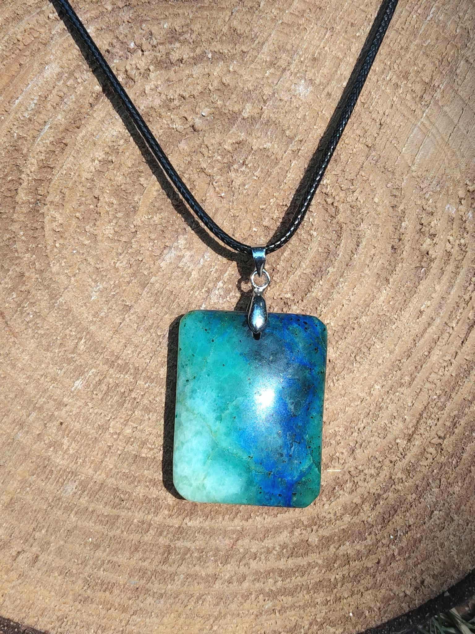Pendentif azurite chrysocolle rectangulaire bleu vert sur cordon noir, présenté sur rondin de bois, pierre naturelle reliée au discernement, à la stabilité émotionnelle et à l’expression sincère.
