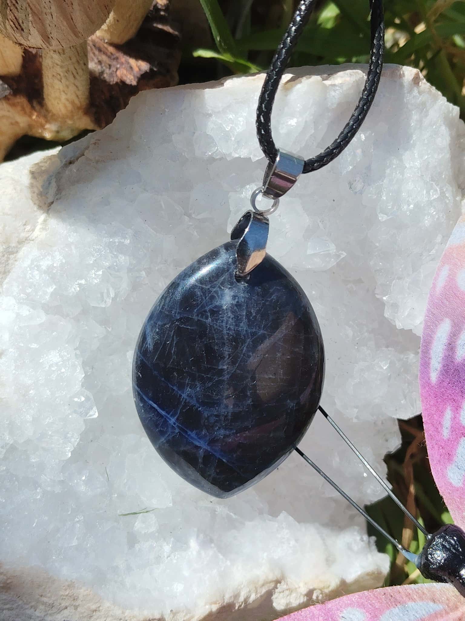 Pendentif sodalite bleue naturelle en forme de feuille sur cordon noir, posé sur amas de quartz, bijou en pierre naturelle associé au discernement, à l’intuition et à l’équilibre intérieur.
