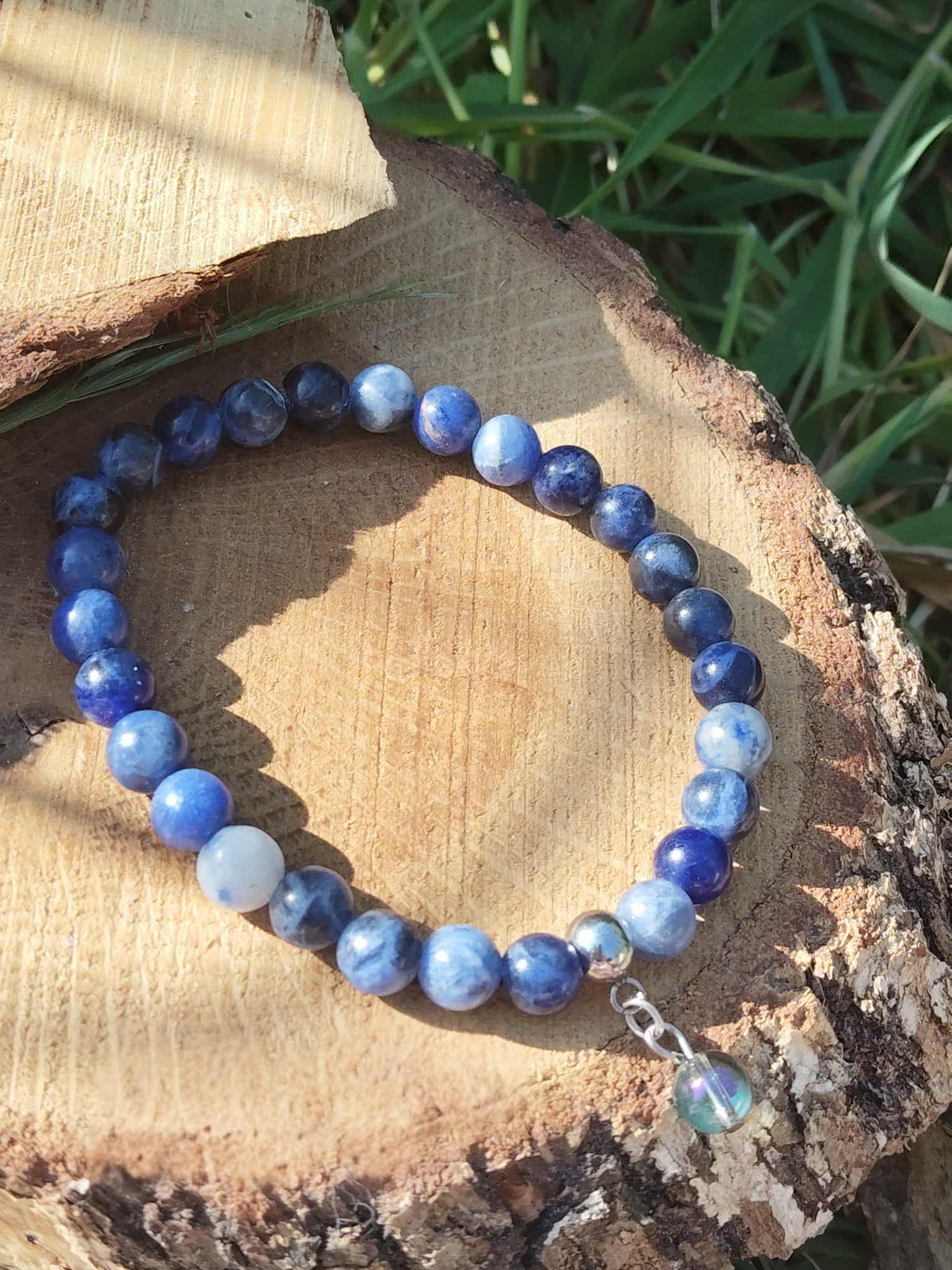 Bracelet sodalite 6 mm sur tranche de bois au soleil avec feuillage vert, perles bleu nuit et bleu ciel pour lucidité et apaisement du mental