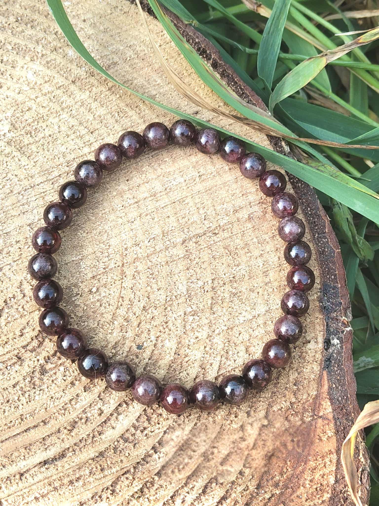 Bracelet grenat 6 mm en perles rondes bordeaux sur tranche de bois en extérieur, détermination, courage enraciné et assurance calme