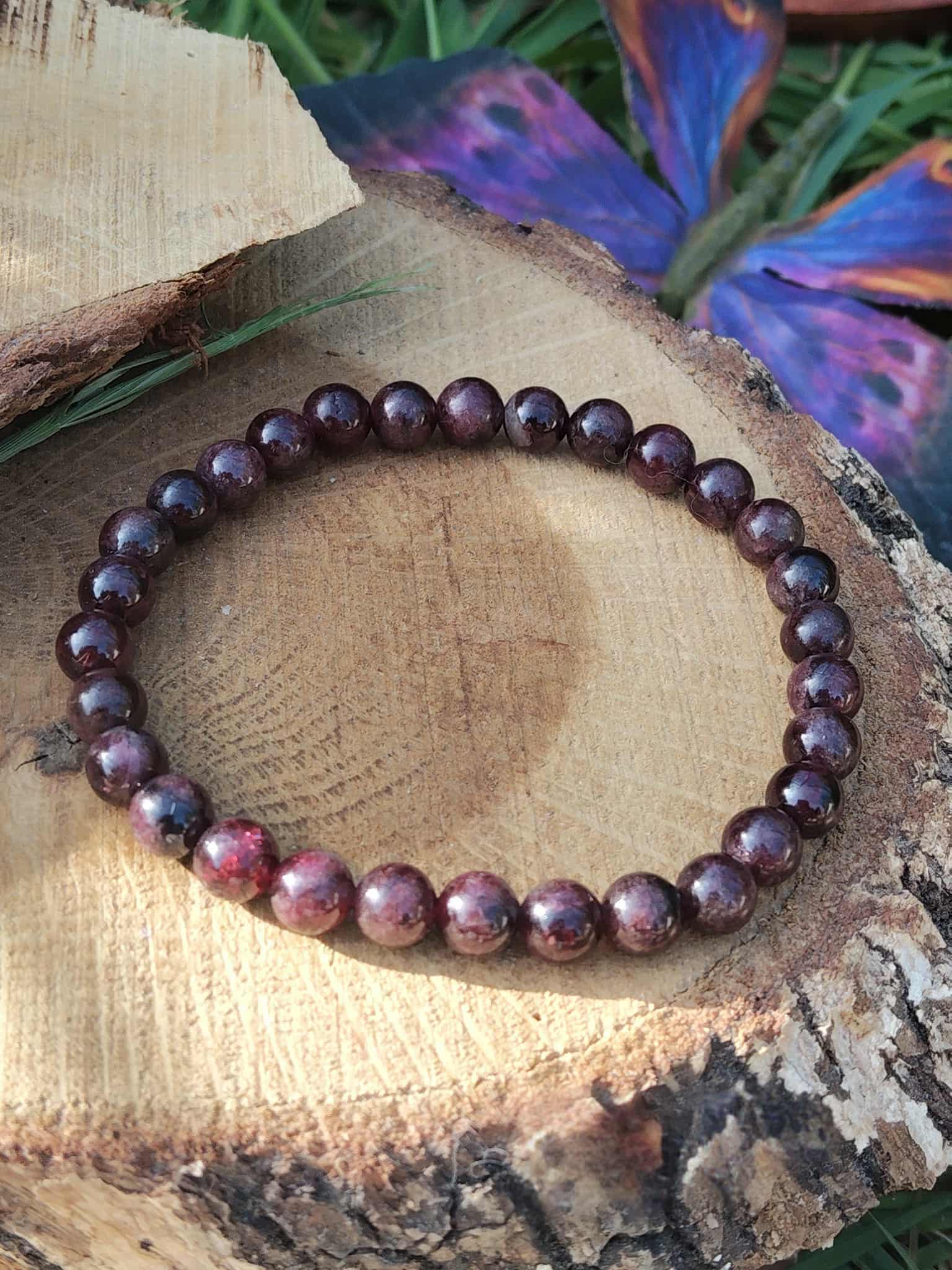 Bracelet grenat 6 mm sur tranche de bois avec fond fleuri, nuances rouge grenat et bordeaux pour motivation, aplomb et rayonnement personnel