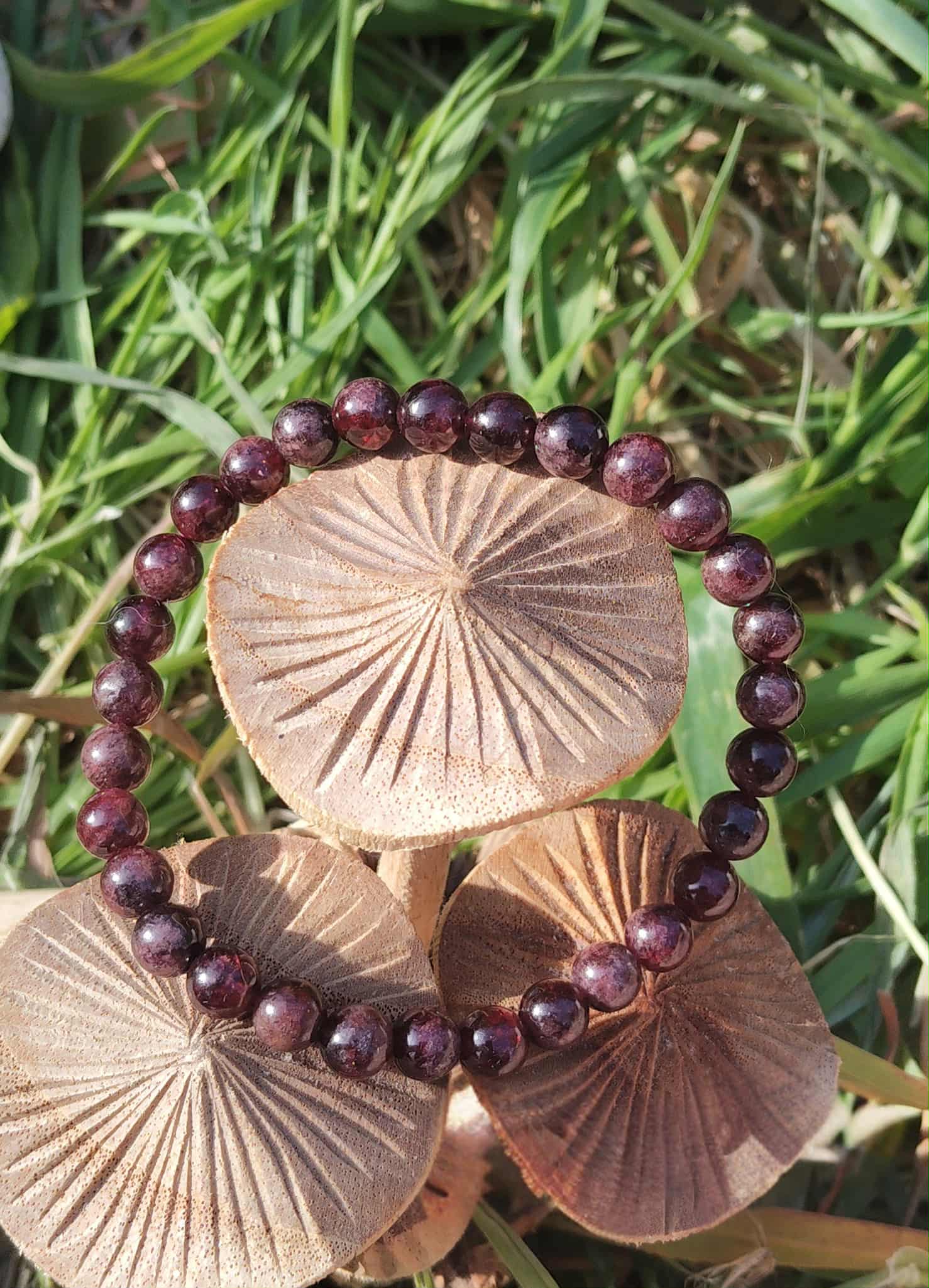 Bracelet grenat 6 mm sur champignons en bois dans l’herbe, perles rouge profond pour courage tranquille, ancrage et stabilité intérieure