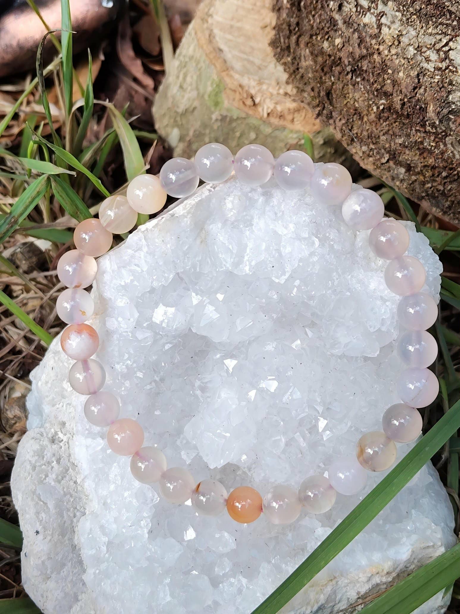 Bracelet en agate fleur de cerisier posé sur géode de cristal blanc avec herbe et pierres, douceur affective et apaisement du mental
