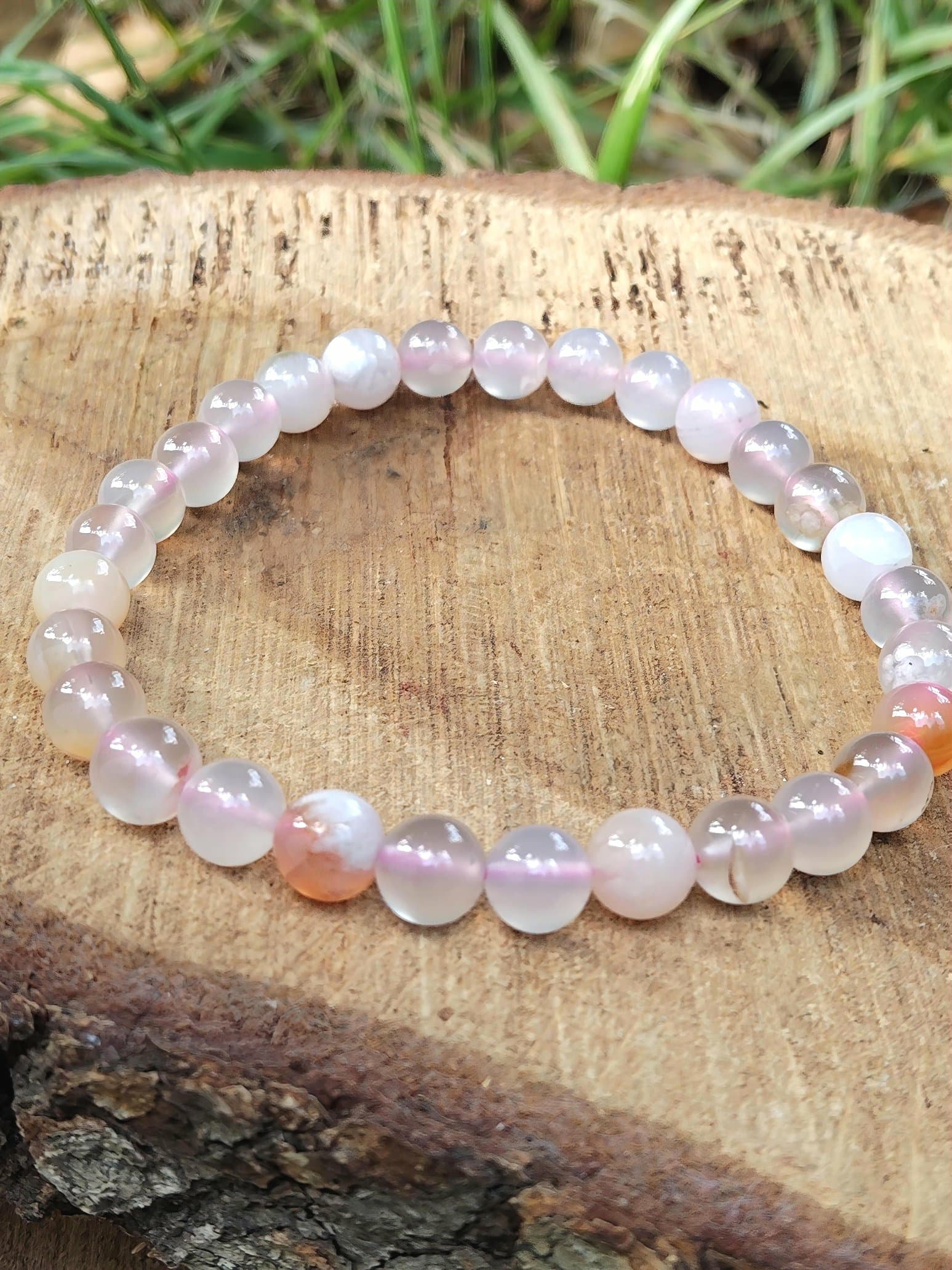 Bracelet en agate fleur de cerisier sur rondin de bois en extérieur, nuances rose poudré pour harmonie du cœur et renouveau personnel