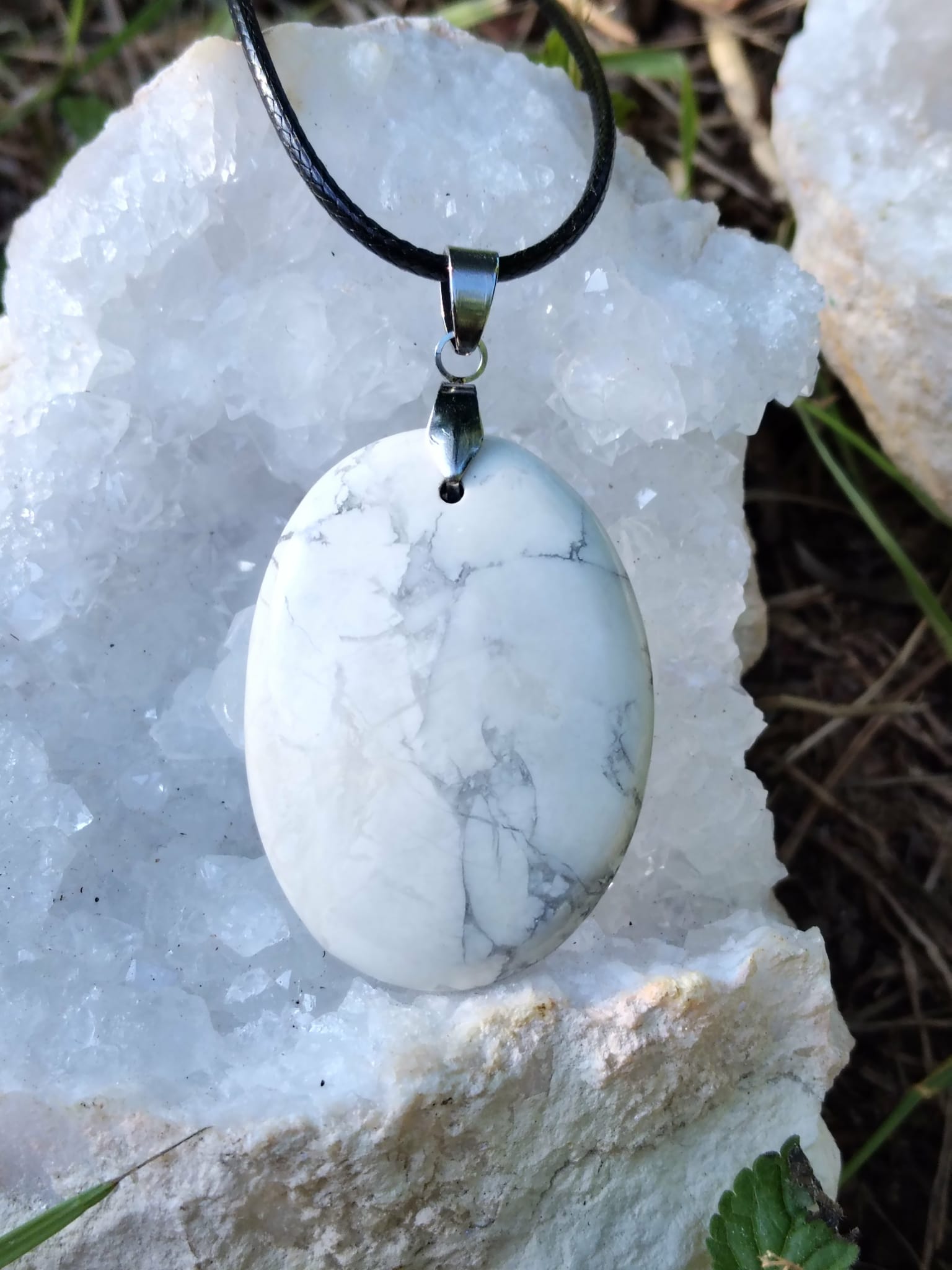 Pendentif howlite blanche sur cordon noir, posé sur amas de quartz en extérieur, calme du mental, détente nerveuse et douceur intérieure