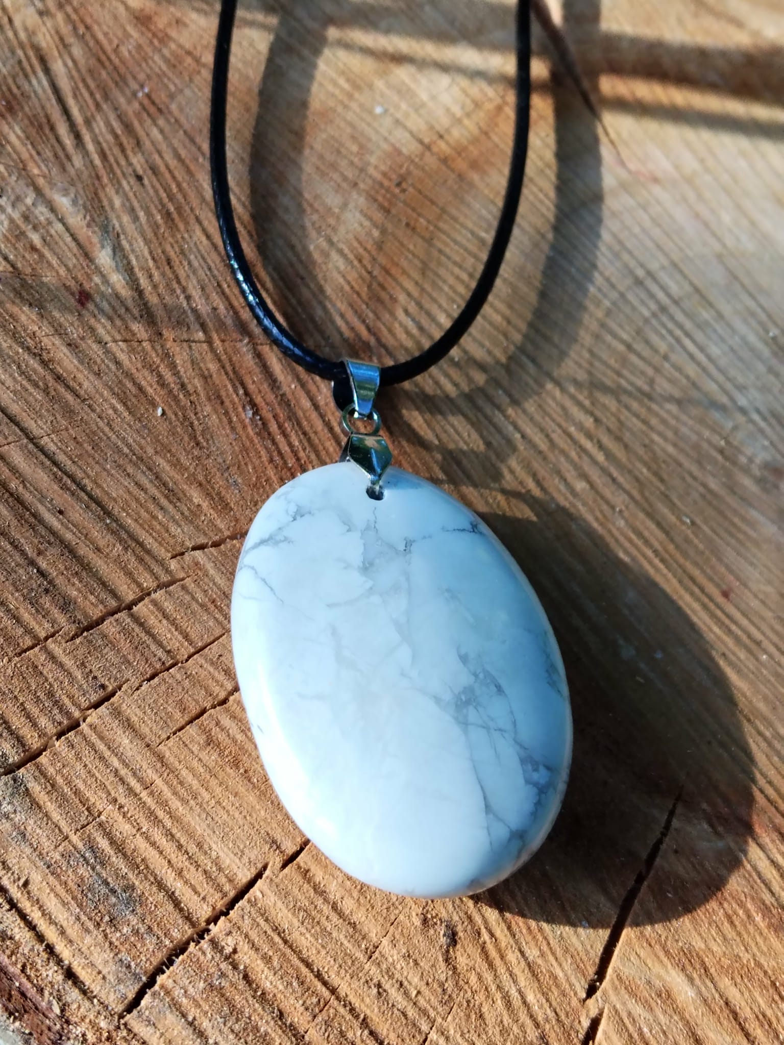 Pendentif disque en howlite blanche sur cordon noir, présenté sur bois, soutien symbolique pour hypersensibilité, tensions nerveuses et périodes de transition