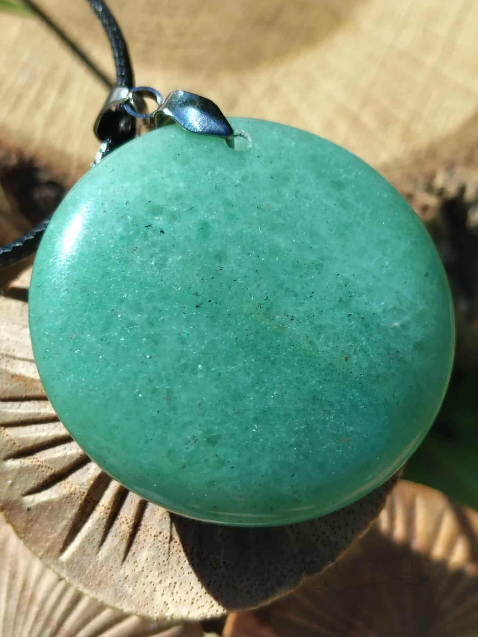 Gros plan sur pendentif aventurine verte poli avec bélière métal et cordon noir, posé sur petits champignons, réconfort émotionnel et énergie apaisée