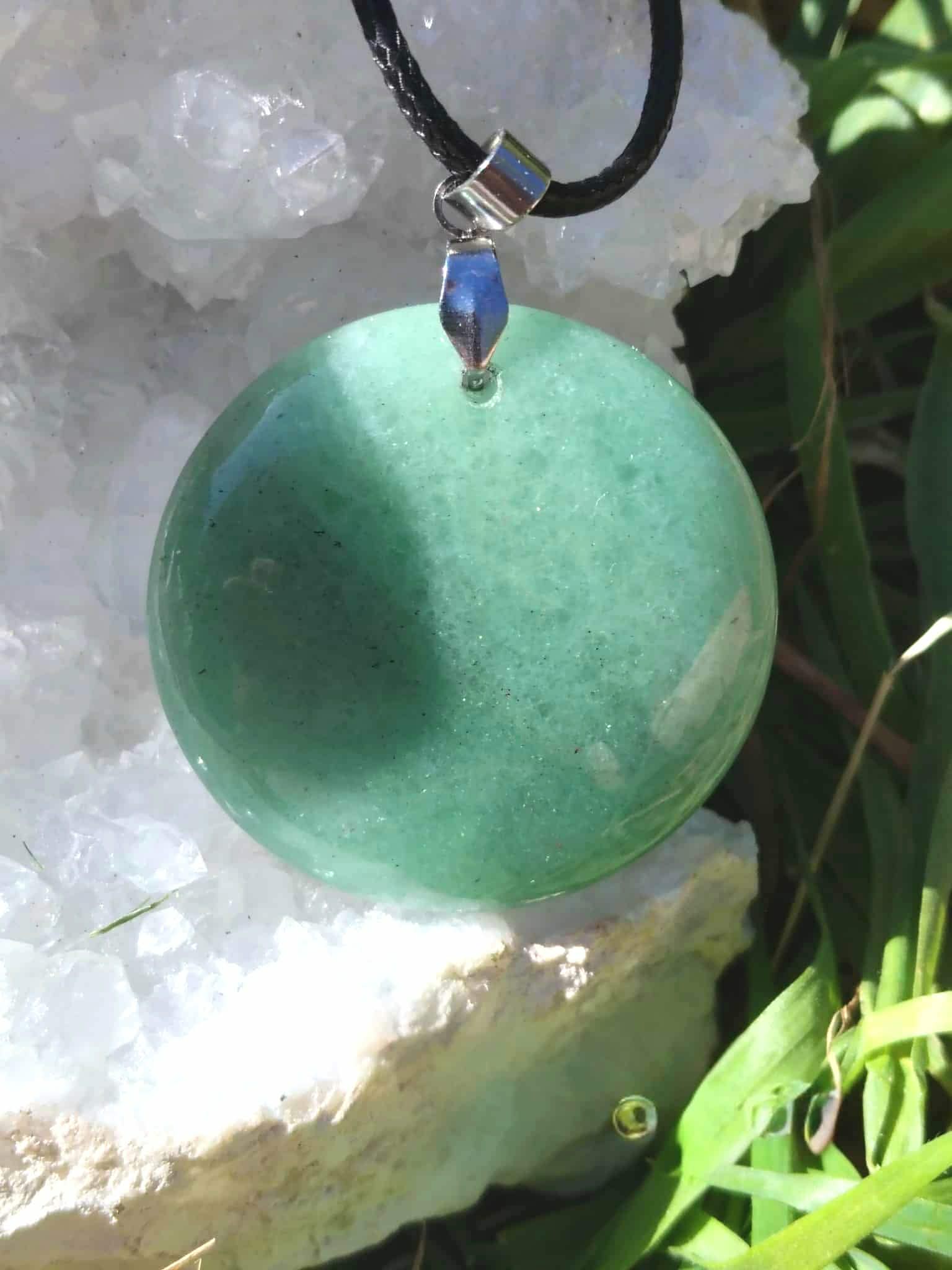 Pendentif disque aventurine verte sur cordon noir, mis en scène sur amas de quartz et verdure, self-control, ancrage doux et ouverture du cœur
