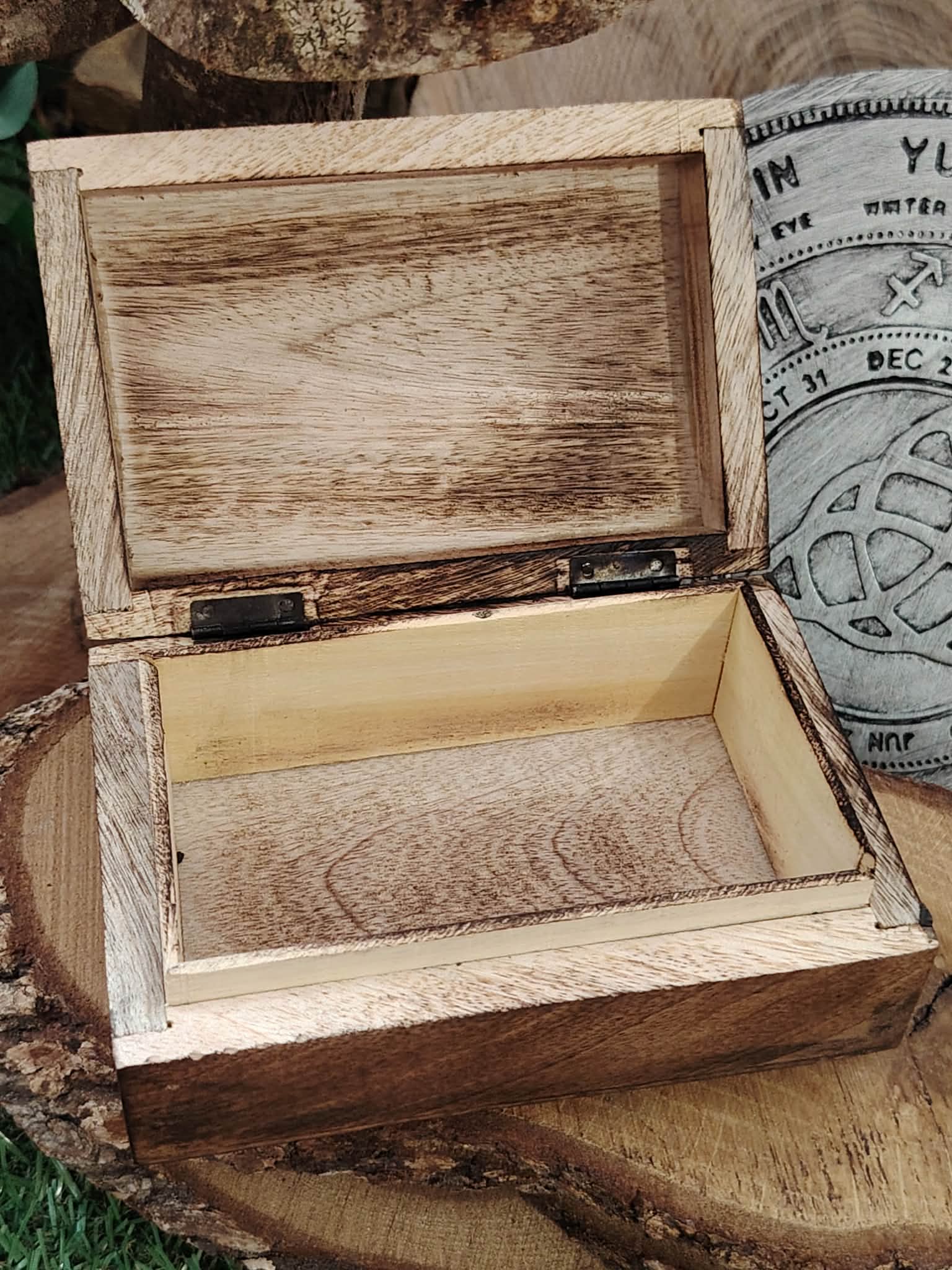 Boîte à bijoux en bois sculpté Gaïa ouverte, montrant l’intérieur en bois brut, posée sur un support naturel.