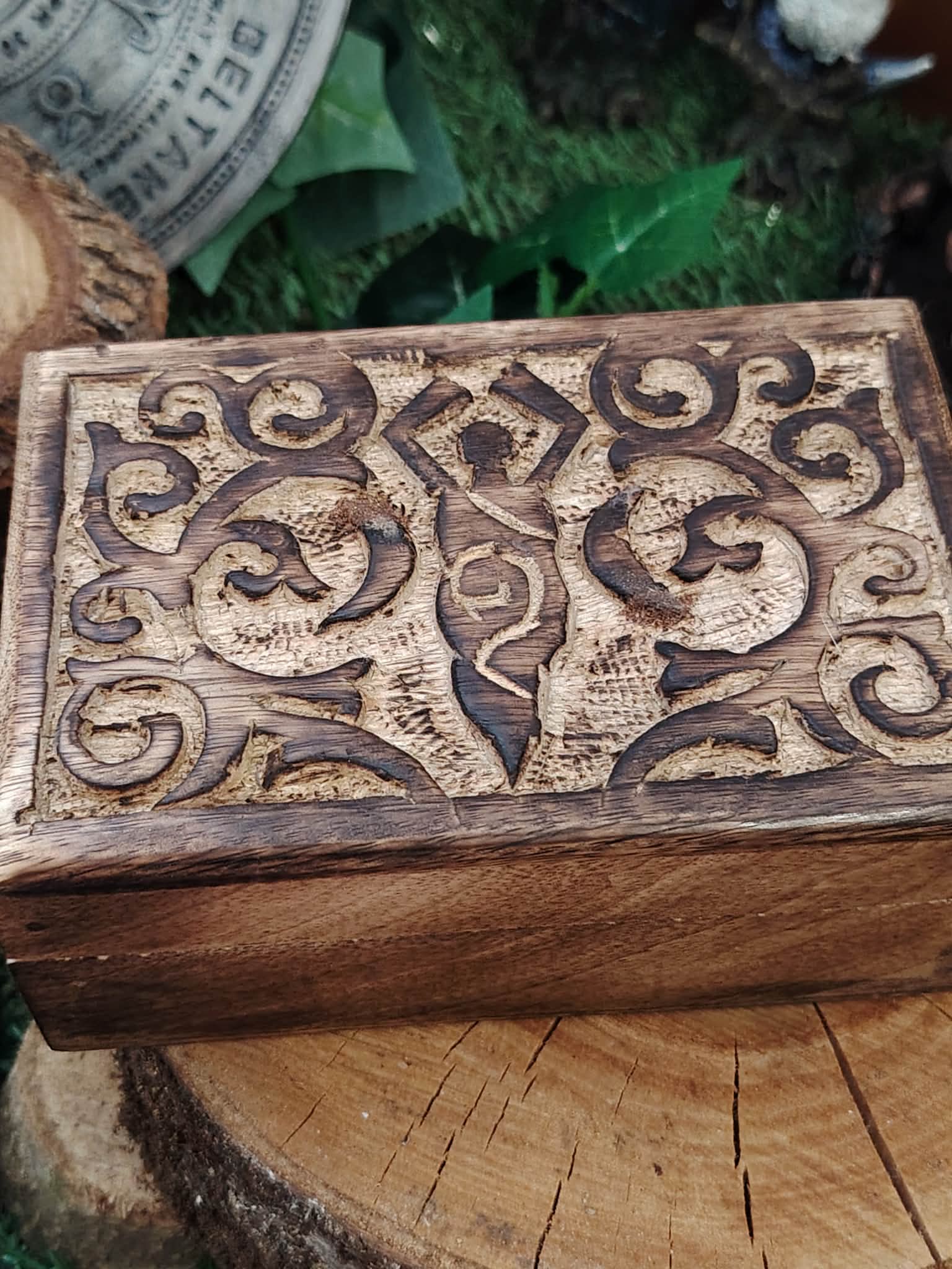 Boîte à bijoux en bois sculpté motif déesse, posée sur une tranche de bois avec du feuillage vert en arrière-plan, pour ranger bijoux et petites pierres.