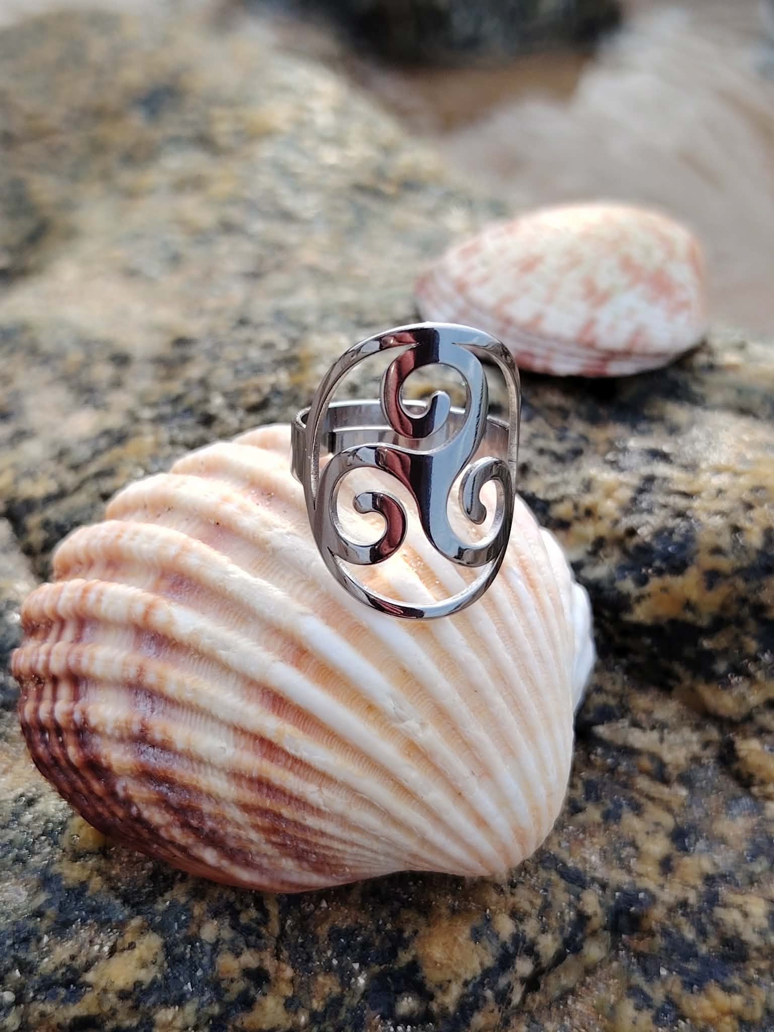 Bague Triskell réglable en acier inoxydable, bijou celtique de protection et d’harmonie posé sur un coquillage sur la plage en Bretagne