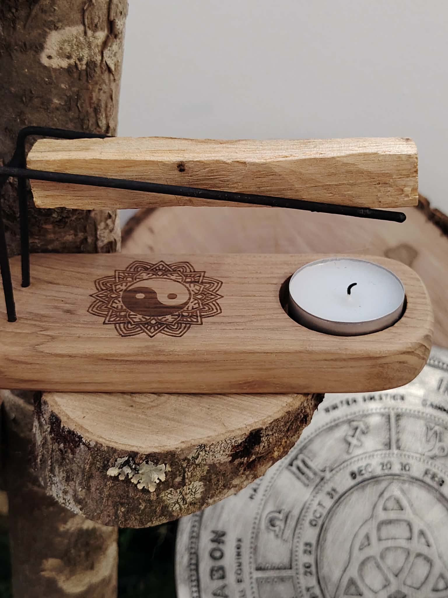 Porte palo santo en bois motif Yin Yang avec bougie chauffe-plat et bâton de palo santo en équilibre sur rondins de bois