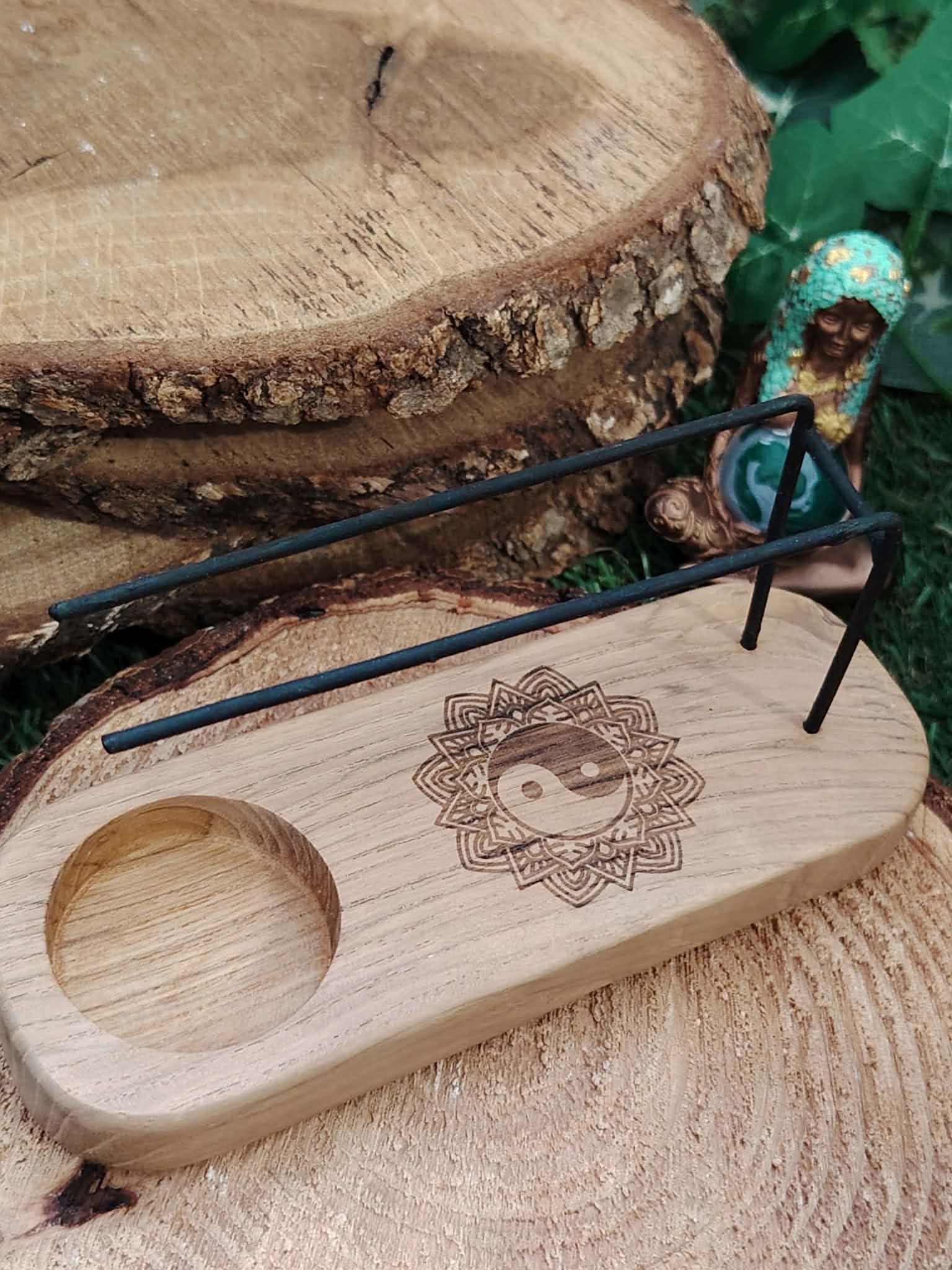 Porte palo santo en bois gravé Yin Yang sur rondins de bois, tiges métalliques visibles, avec statuette déesse et verdure en arrière-plan – Magic Gaïa