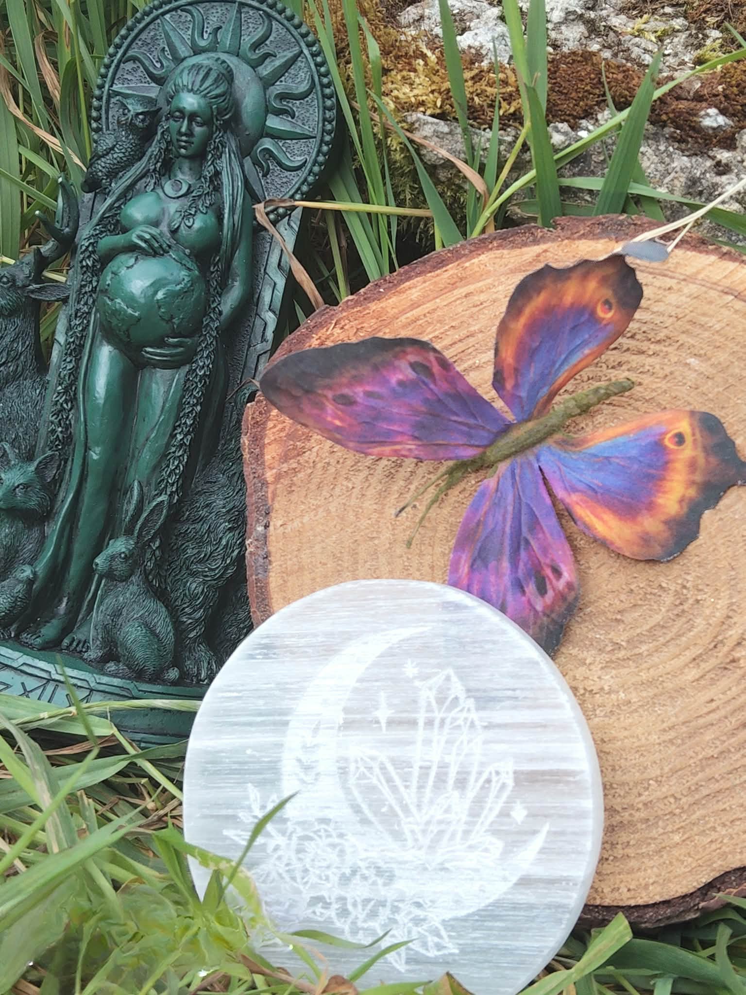 Plateau rond en sélénite blanche 10 cm, posé dans l’herbe avec statue de Gaïa, idéal pour recharger cristaux et harmoniser les émotions