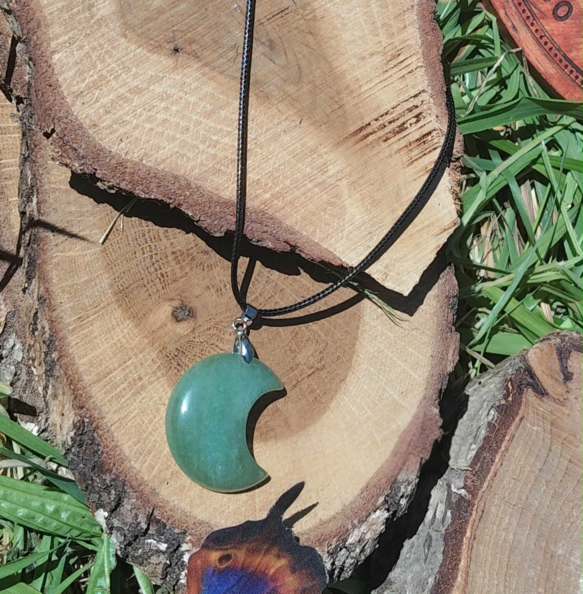 Pendentif lune en aventurine verte sur rondin de bois, bijou en pierre naturelle lié à la maîtrise de soi, à l’apaisement et à la stabilité émotionnelle.