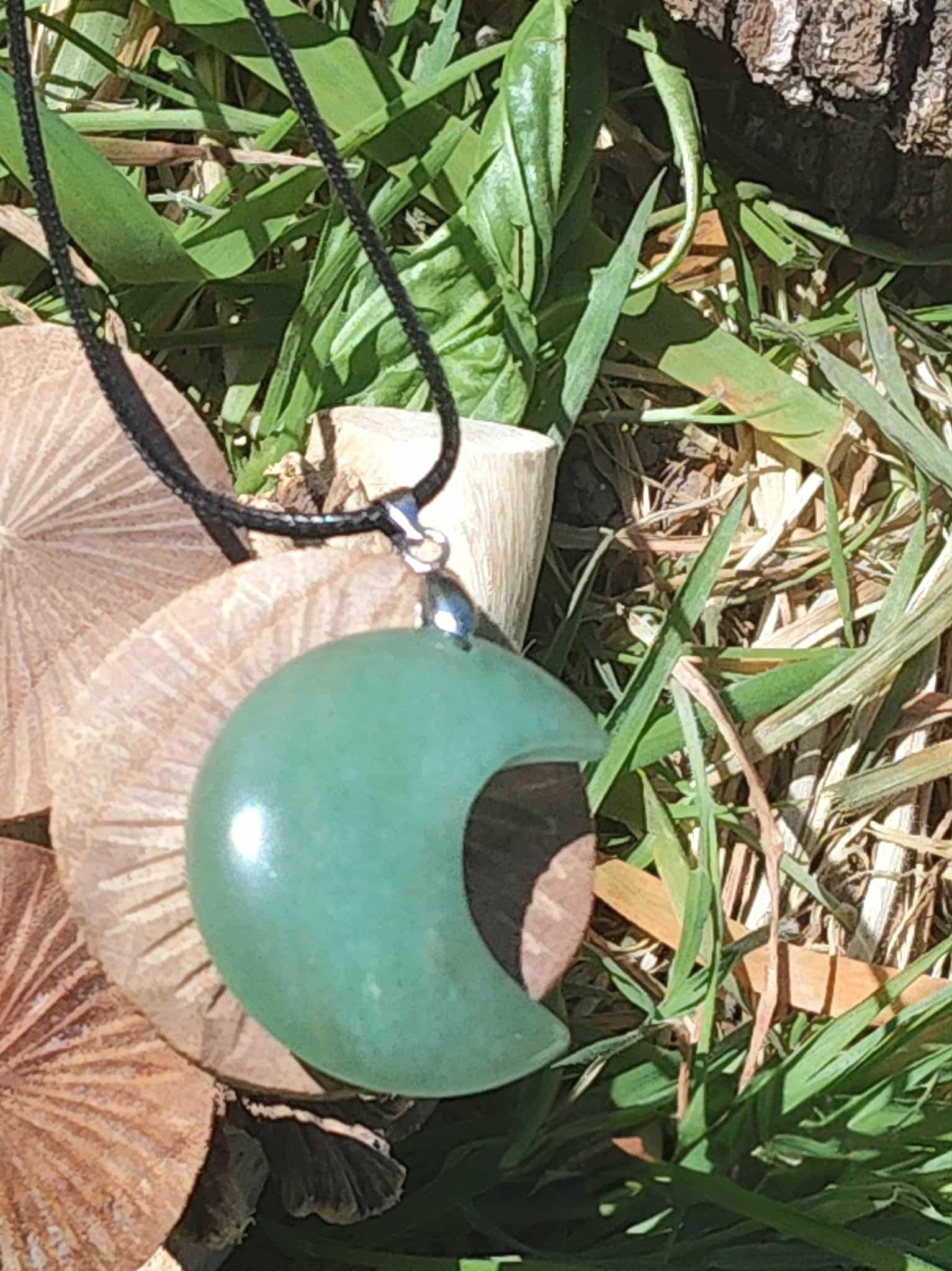 Pendentif lune en aventurine verte posé sur champignon et herbe, bijou en pierre naturelle évoquant la tranquillité, la patience et la douceur relationnelle.