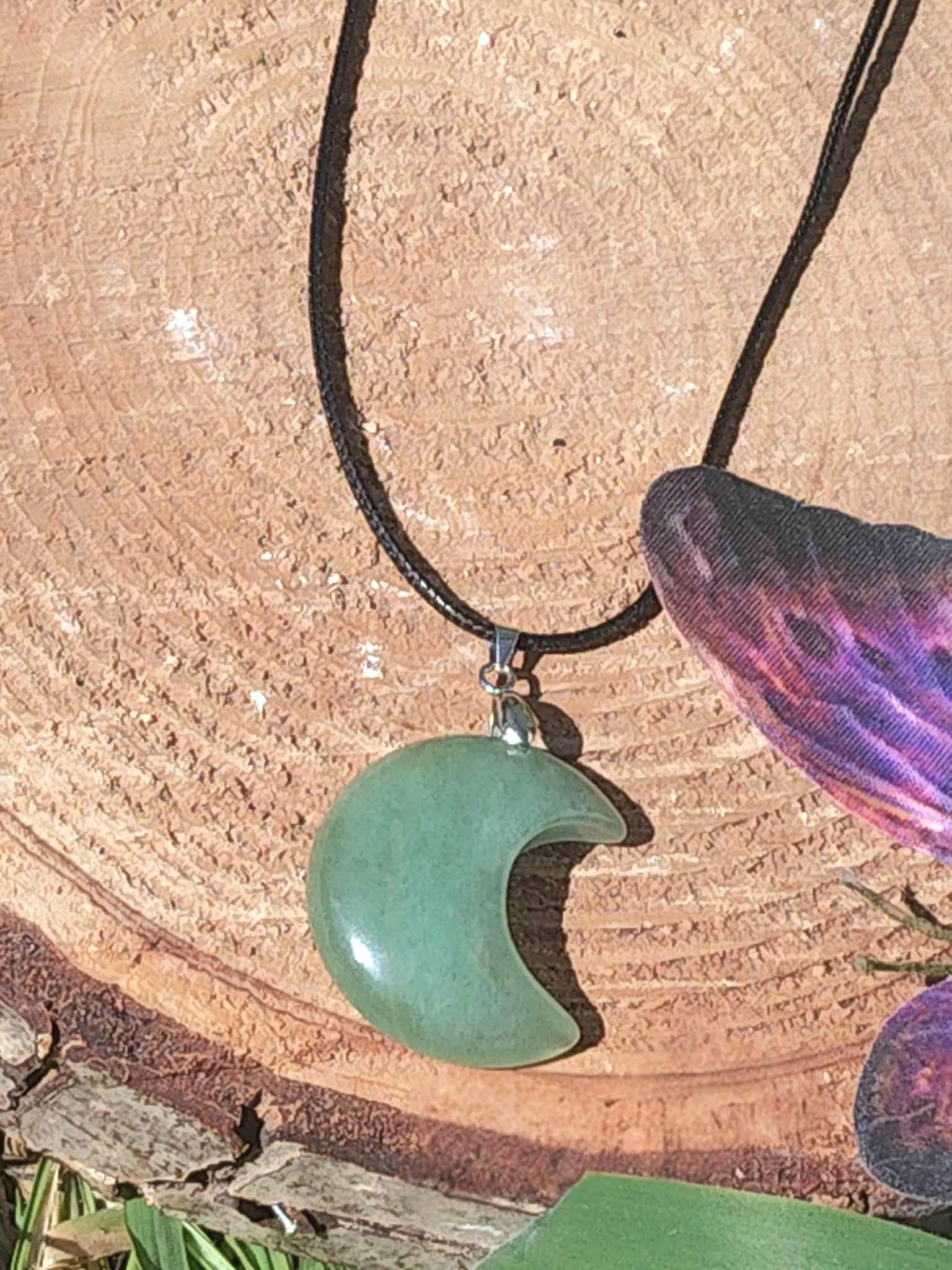 Pendentif lune en aventurine verte sur rondin de bois avec plume, pierre naturelle associée à l’apaisement du cœur, à la souplesse émotionnelle et au calme intérieur.