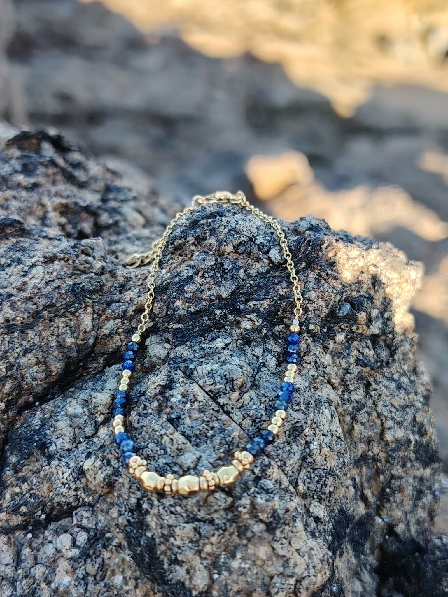 Bracelet perles lapis lazuli facettées et détails dorés, acier inoxydable résistant à l’eau, photo sur rocher