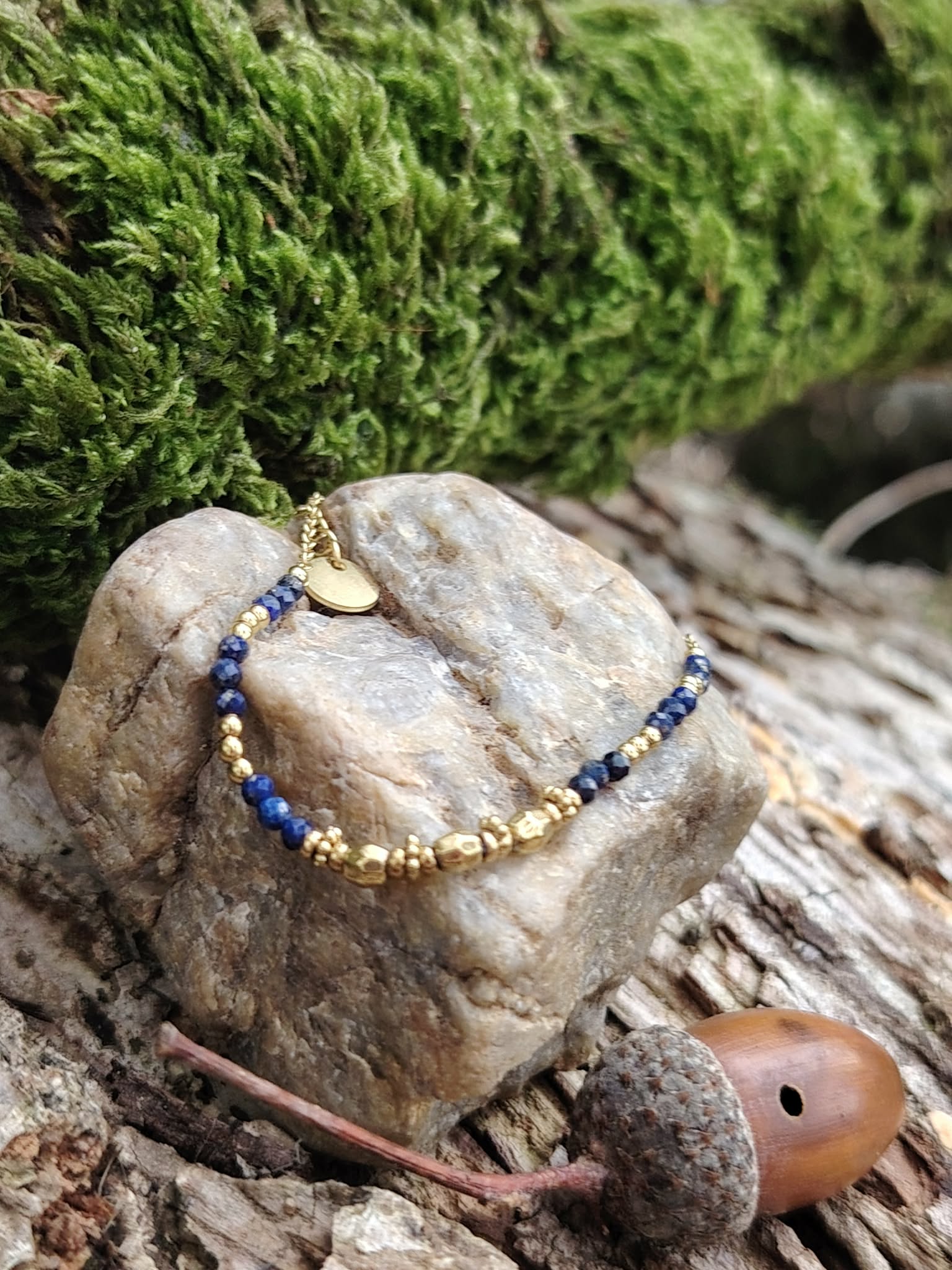 Bracelet chaîne fine dorée avec pierre naturelle bleue (lapis lazuli), posé sur mousse et bois en Bretagne