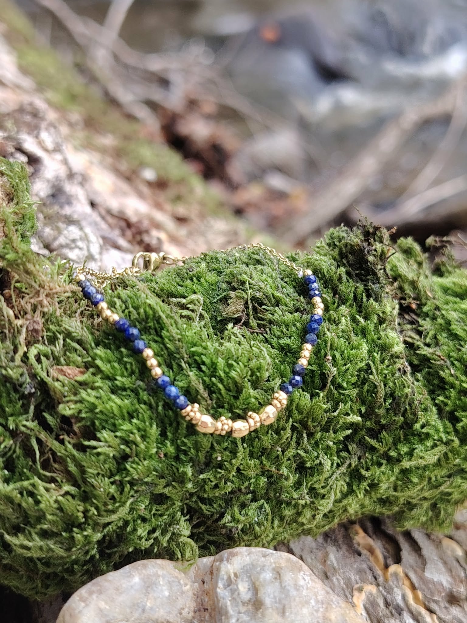 Bracelet chaîne fine dorée avec pierre naturelle bleue (lapis lazuli), posé sur mousse et bois