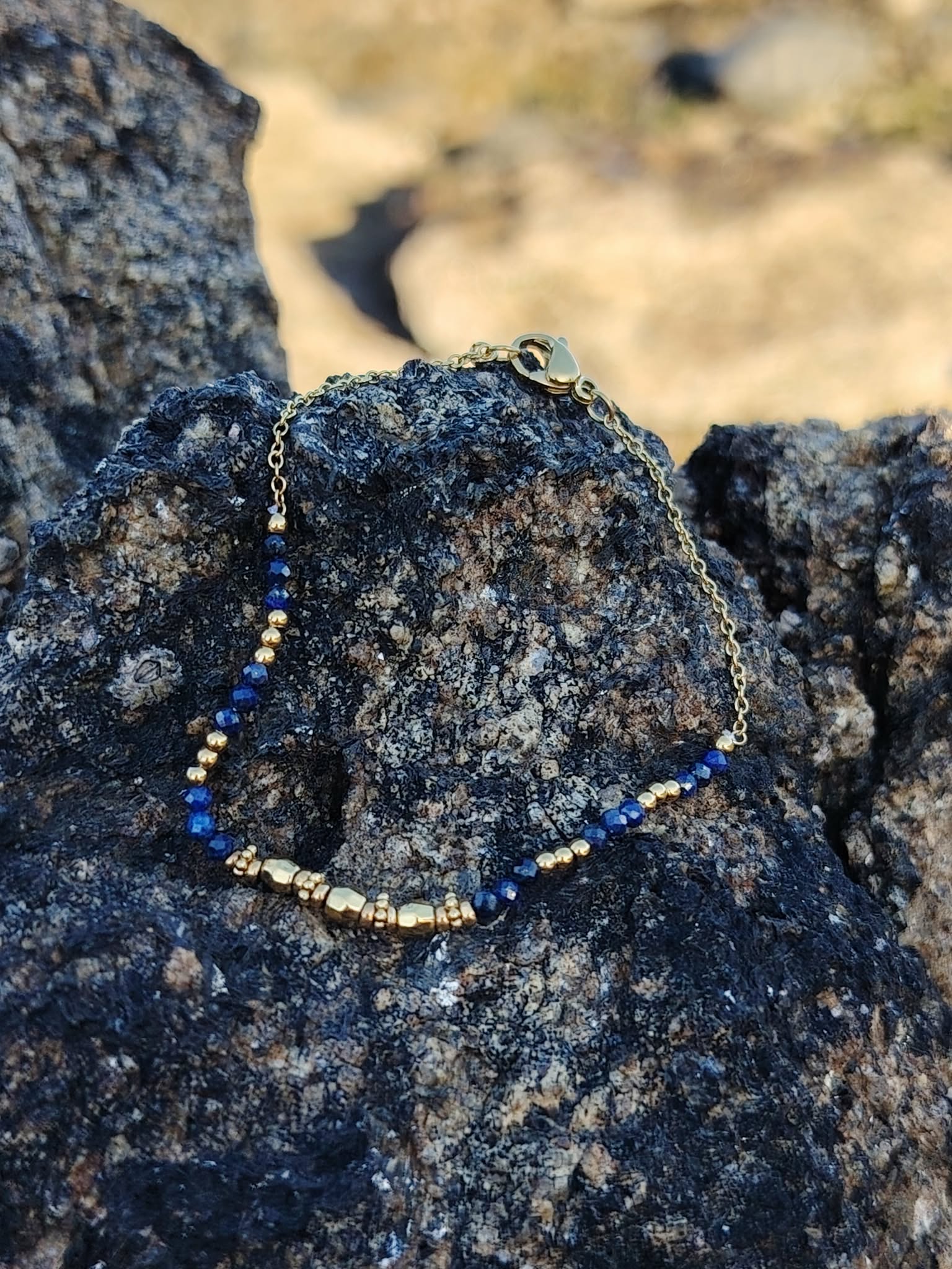 Bijou pierre naturelle bleue lapis lazuli sur chaîne fine dorée, photo lifestyle sur rocher au bord de mer en Bretagne