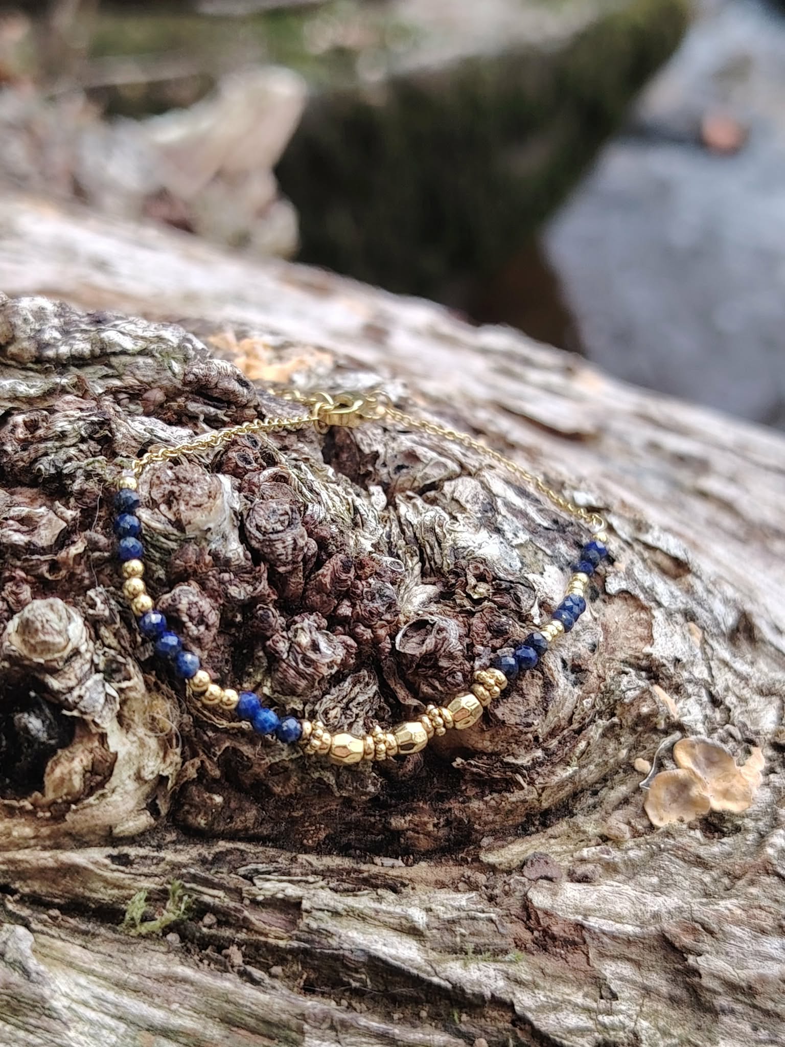 Bracelet chaîne fine doré acier inoxydable avec perles de lapis-lazuli sur bois brut, photo en extérieur Bretagne