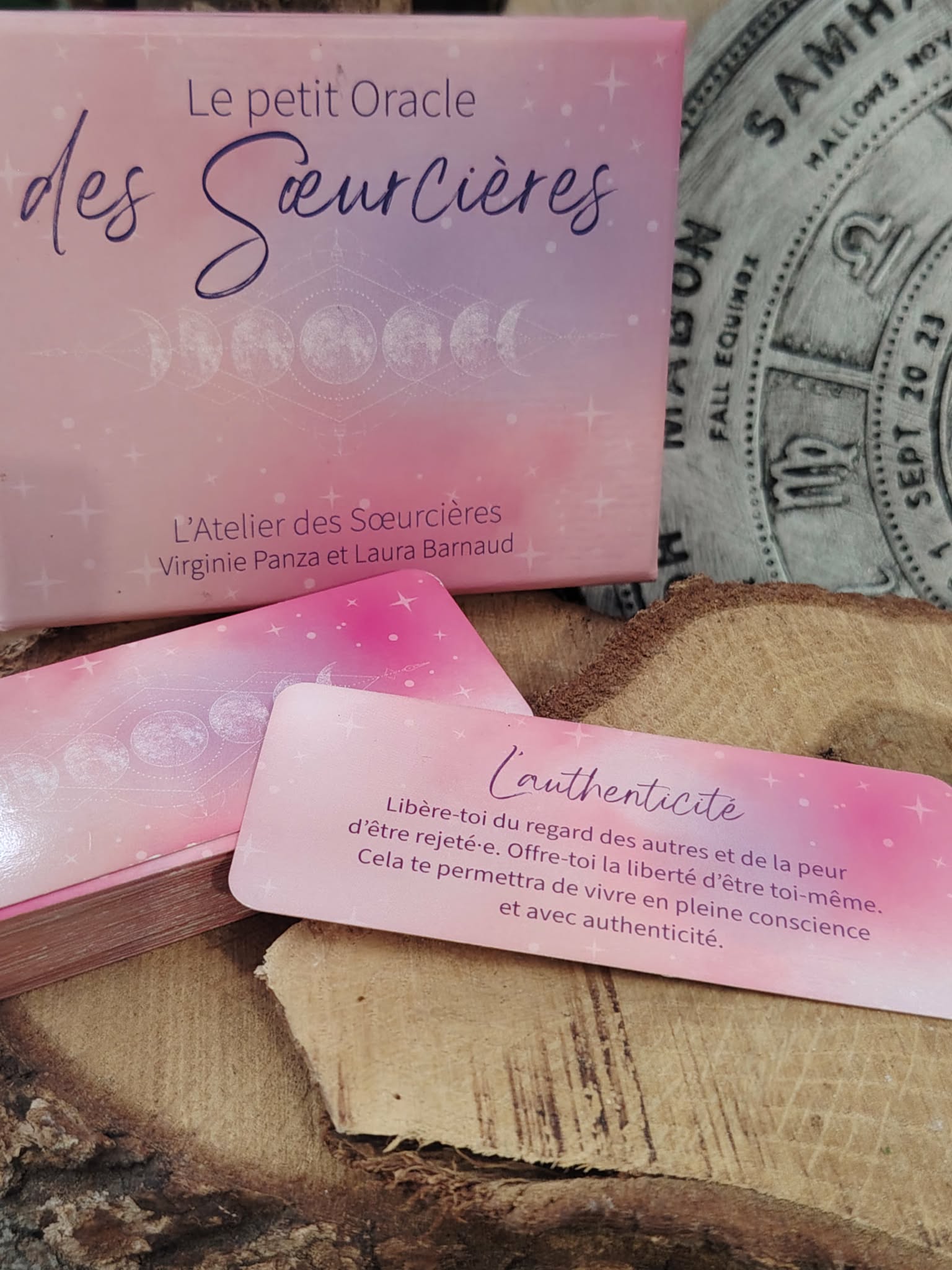 Carte “Augmente tes vibrations” du Petit Oracle des Sœurcières (L’Atelier des Sœurcières) : carte rose avec message inspiration, coffret en arrière-plan sur rondins de bois, décor mandala ésotérique