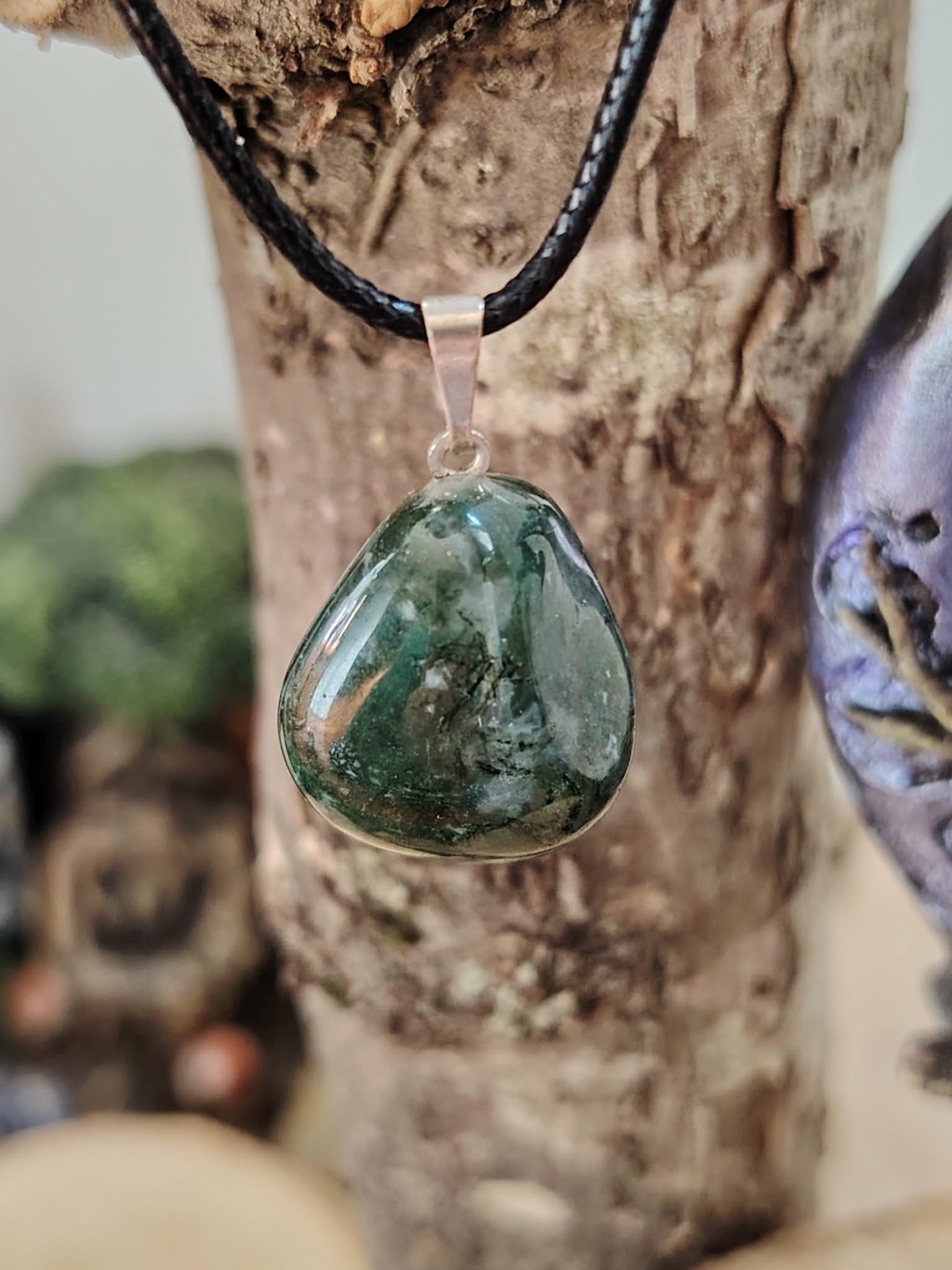 Pendentif agate mousse vert mousse sur cordon noir, photographié devant bois brut et écorce, apaisement mental et respiration intérieure