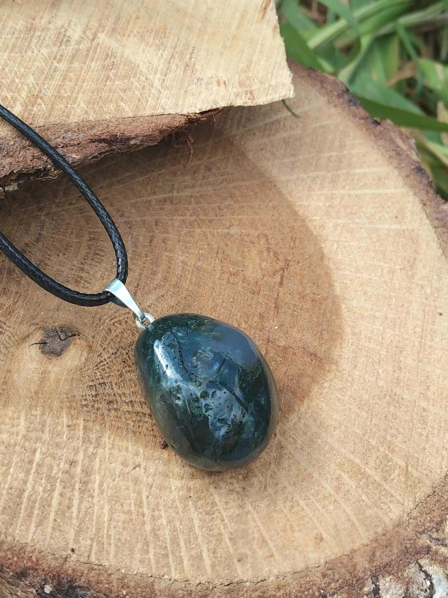Pendentif agate mousse sur cordon noir, décor bois brut avec touche de vert en fond, connexion au vivant et harmonie intérieure