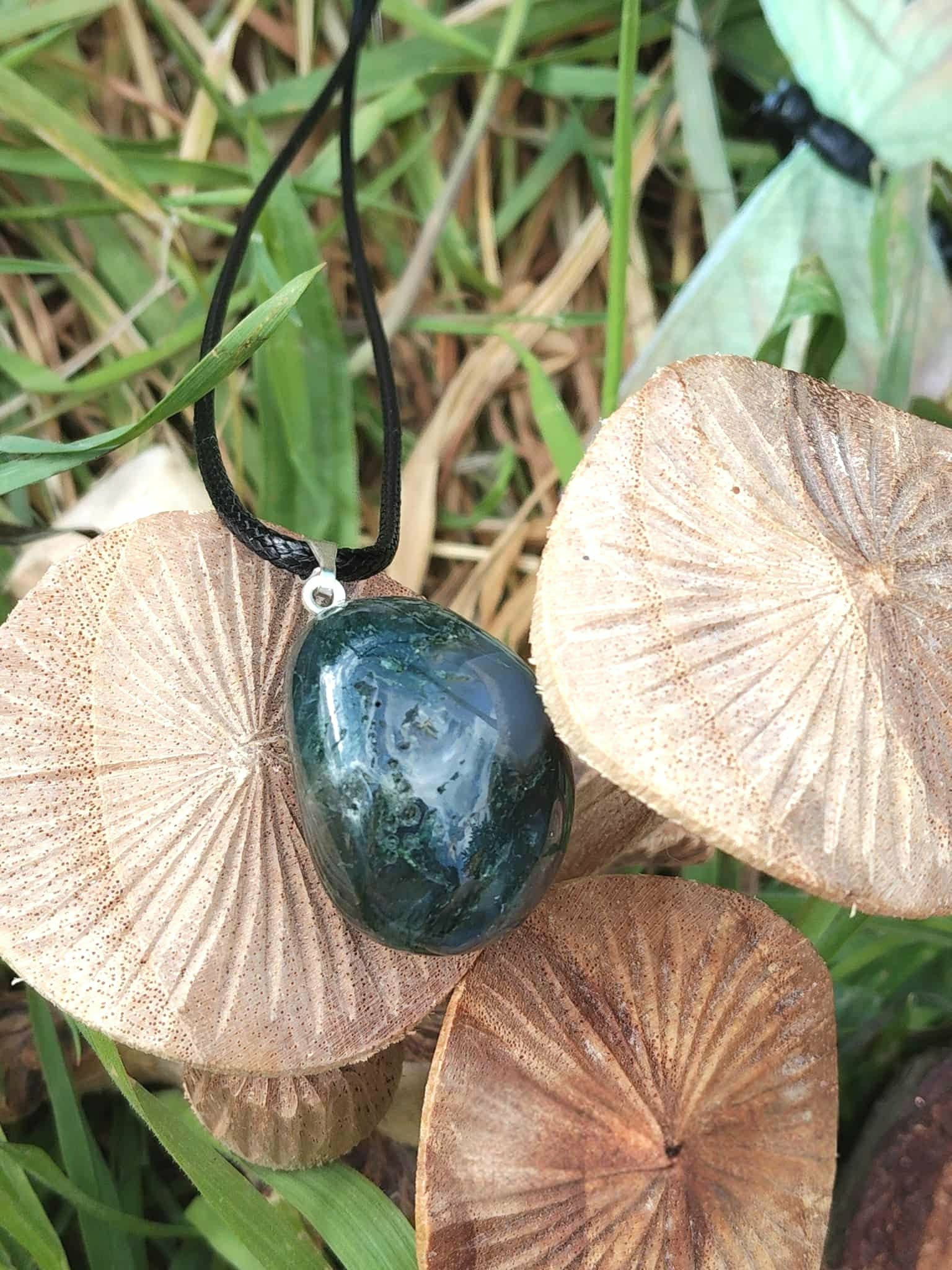 Pendentif agate mousse vert-bleuté sur cordon noir, posé sur coquillages dans l’herbe, apaisement du ressenti et lien au vivant