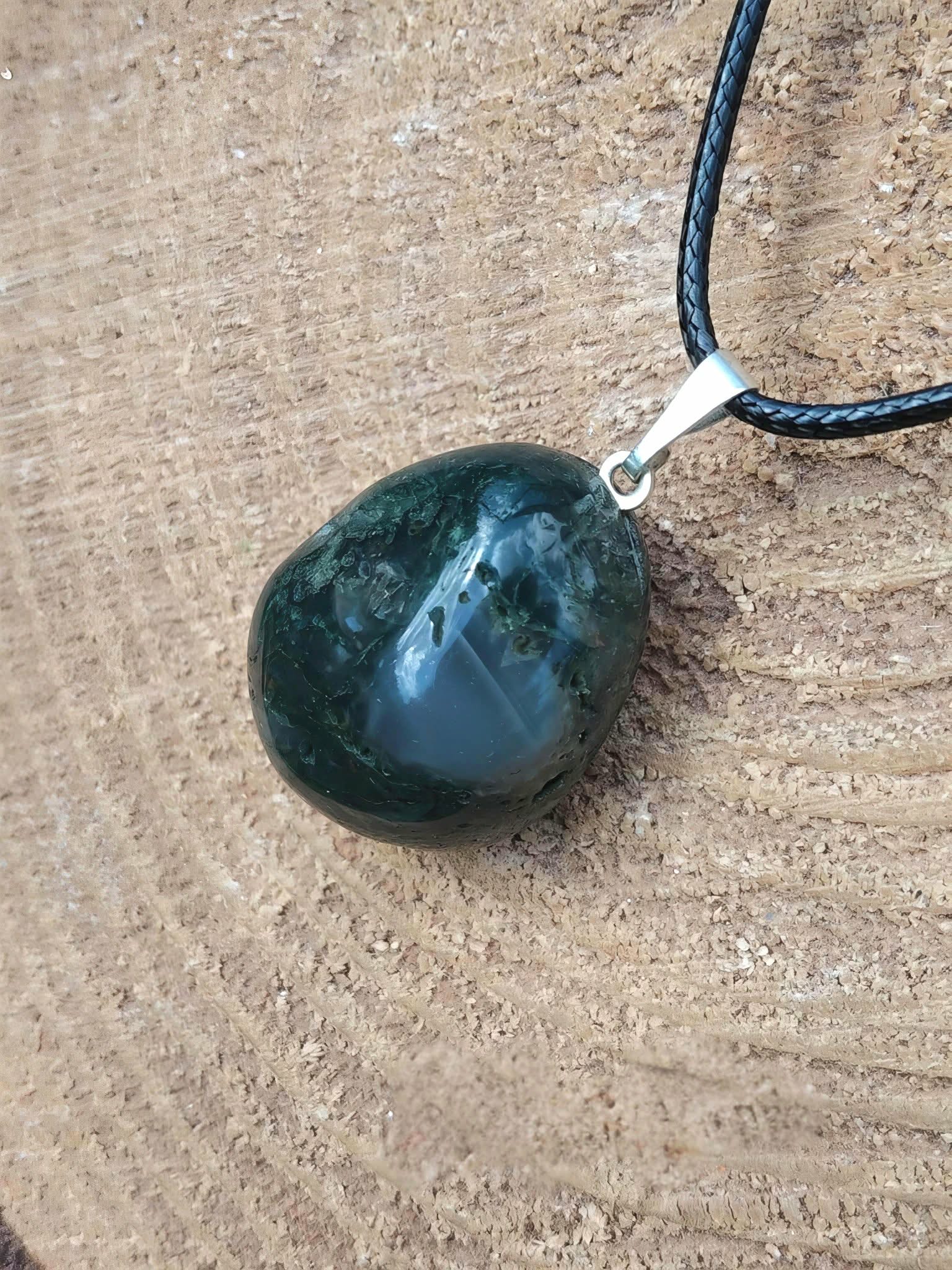 Pendentif agate mousse vert foncé sur cordon noir, posé sur bois brut, ancrage doux et calme du cœur