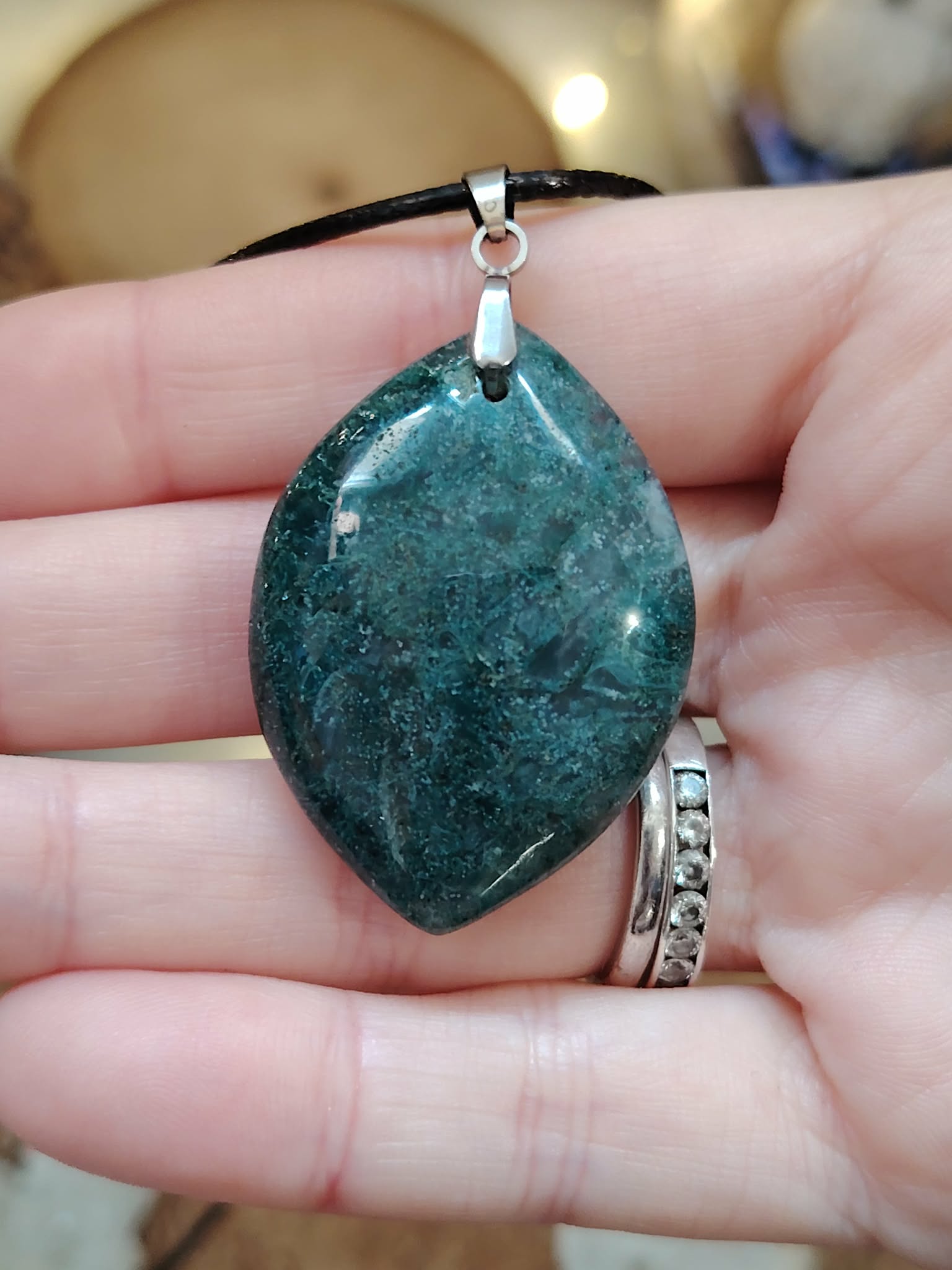 Pendentif agate mousse (goutte) sur cordon noir, sur tranche de bois avec feuillage ; apporte calme et équilibre.