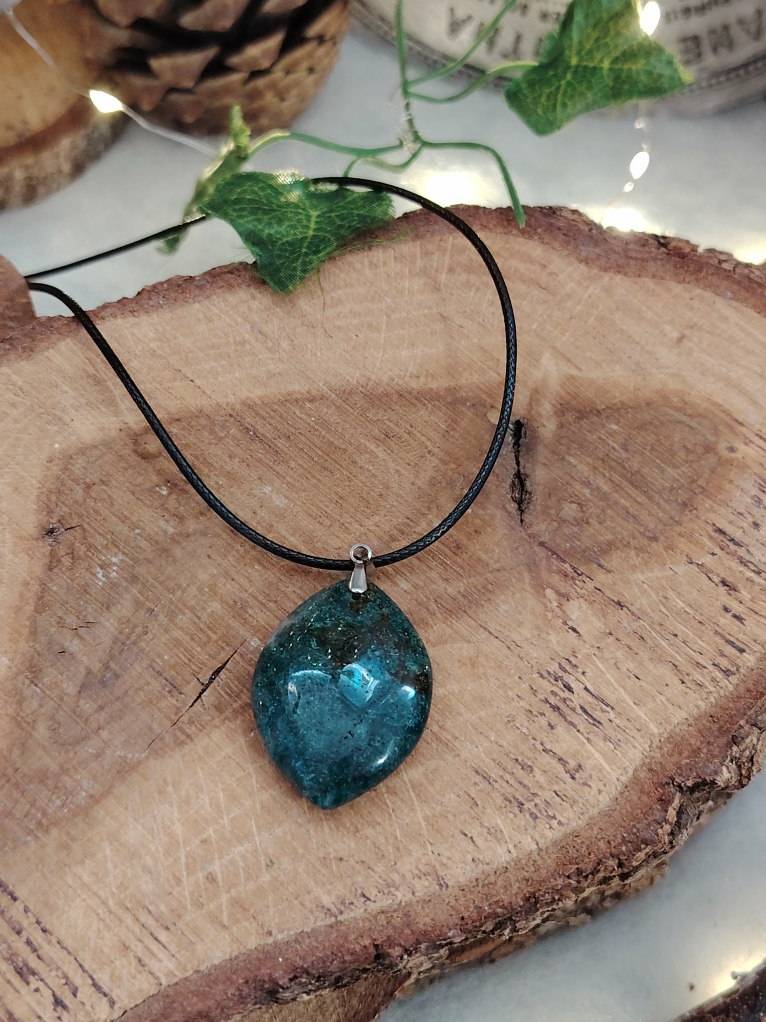 Pendentif agate mousse (goutte) sur cordon noir, sur tranche de bois avec feuillage ; apporte calme et équilibre.