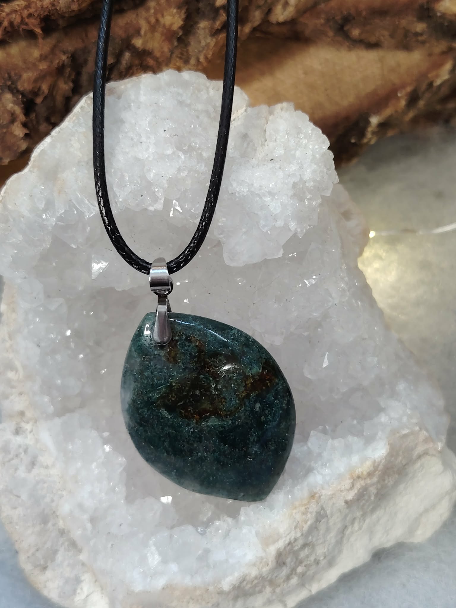 Pendentif agate mousse sur cordon noir, posé sur un amas de quartz; favorise apaisement et harmonie.