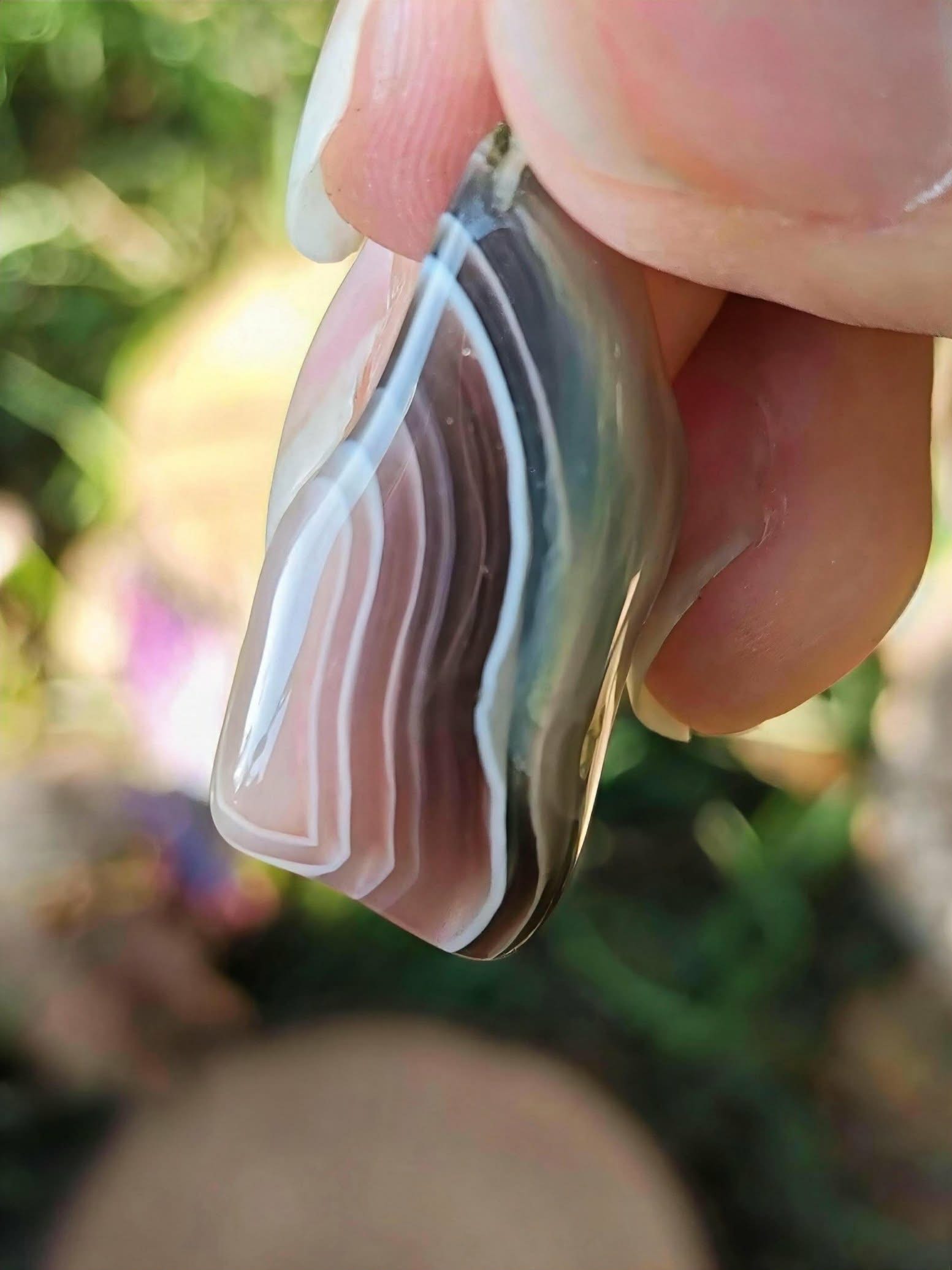 Pendentif agate du Botswana à bandes grises et roses en gros plan dans la main, sérénité émotionnelle et présence apaisée