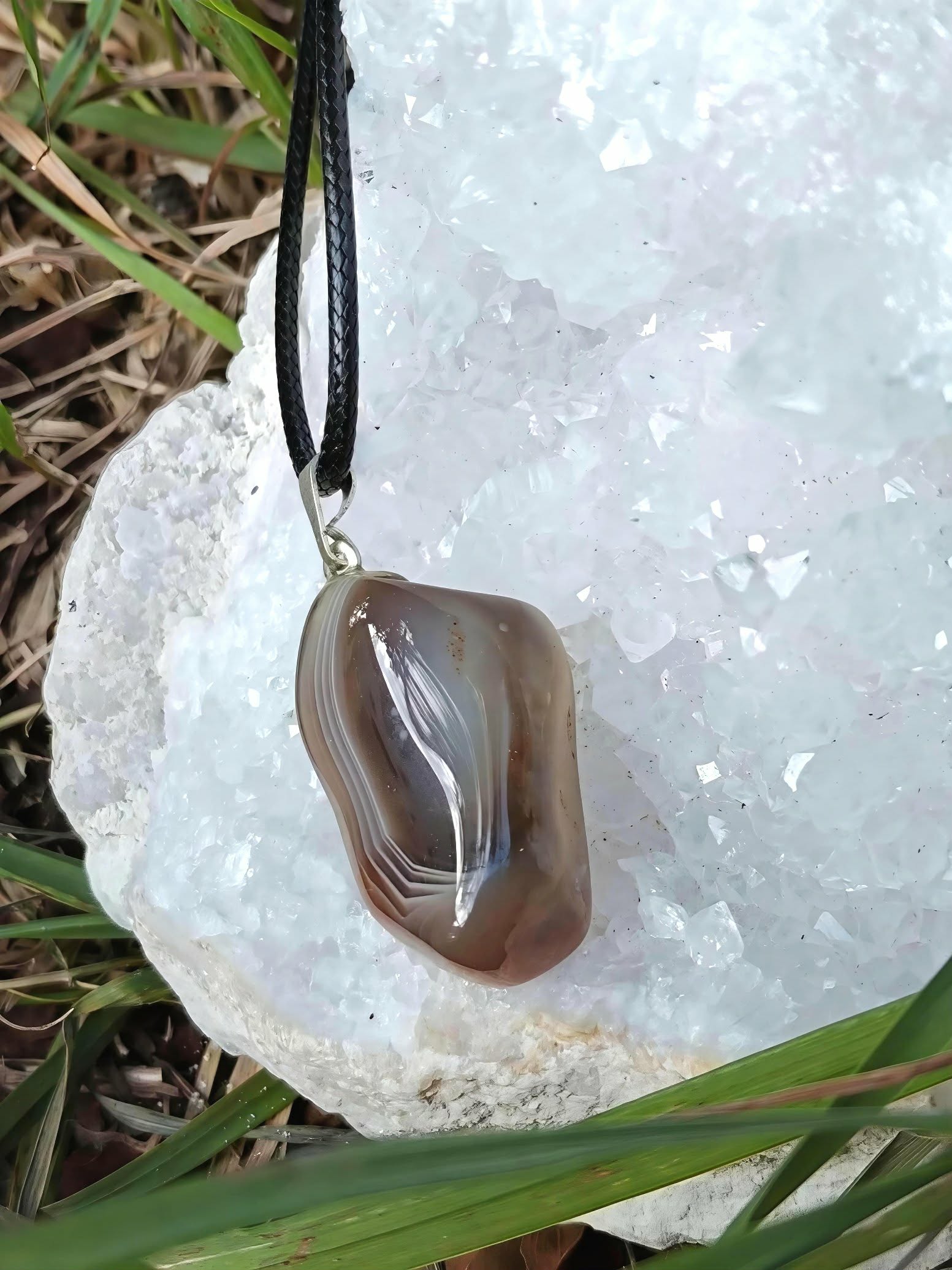 Pendentif agate du Botswana sur druse de quartz blanc dans l’herbe, pierre naturelle pour apaisement émotionnel et relâchement du mental