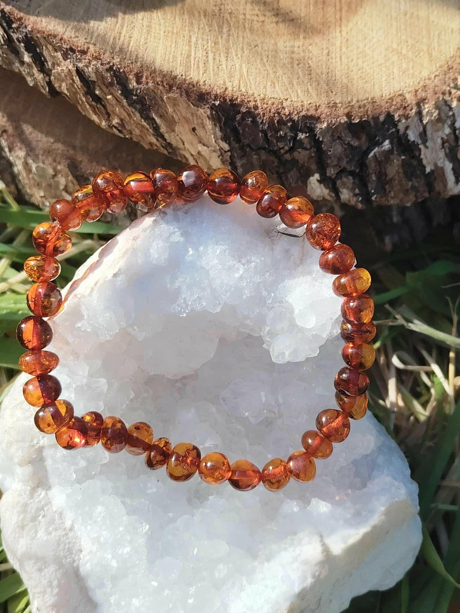 Bracelet ambre sur tranche de bois avec feuille verte et amas de quartz, ancrage lumineux, détente et sensation de cocon