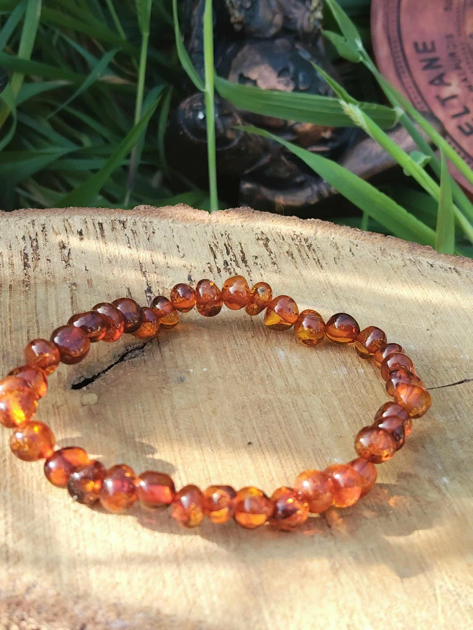 Bracelet ambre naturel posé sur support clair avec feuillage vert en fond, sérénité douce, réassurance et lumière intérieure