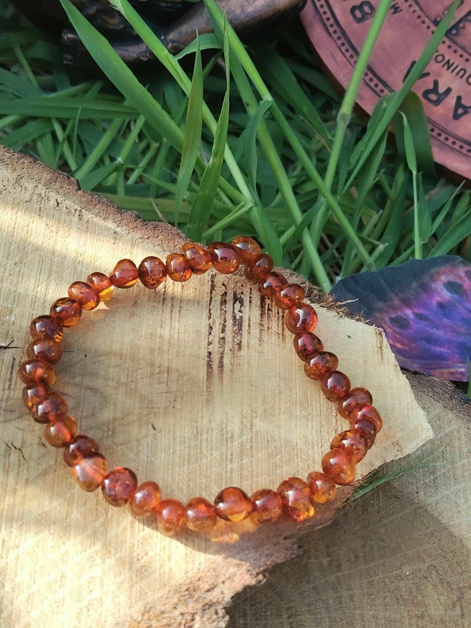 Bracelet ambre naturel couleur cognac sur fond clair avec plantes en arrière-plan, bien-être, vitalité douce et apaisement du mental