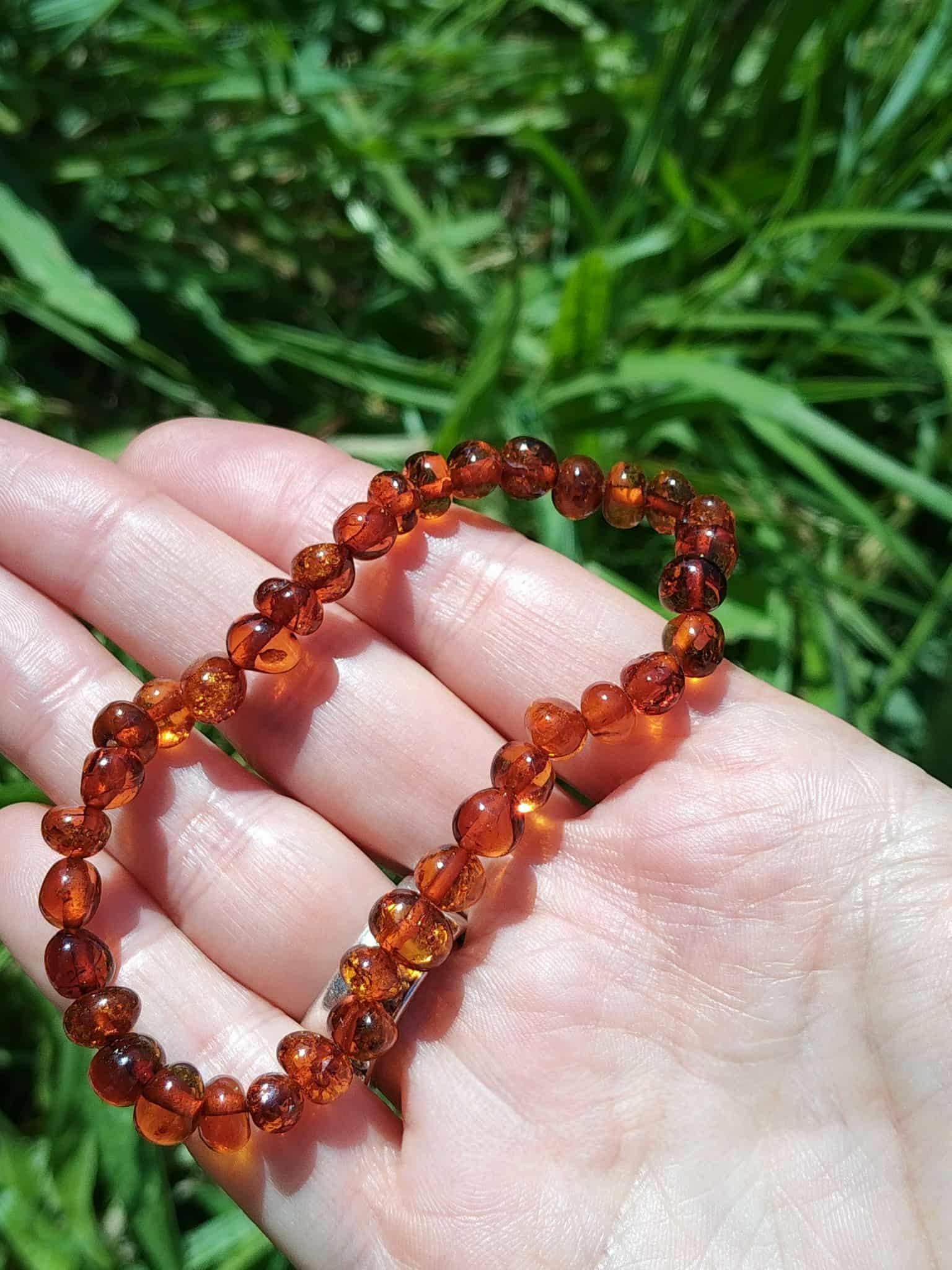 Bracelet d’ambre dans la main avec arrière-plan verdoyant, soutien émotionnel, détente nerveuse et humeur plus stable
